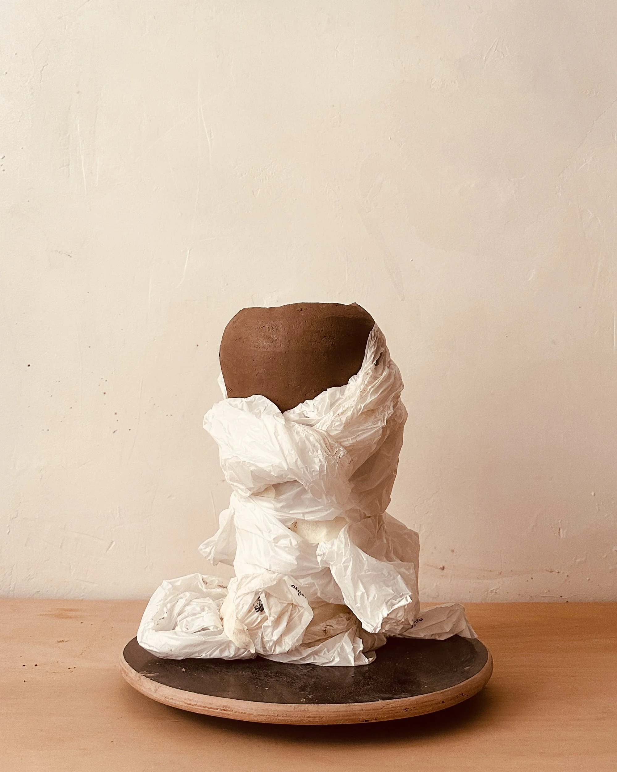 Une sculpture représentant une figure humaine faite avec des morceaux de papier froissé, posée sur un plateau en bois