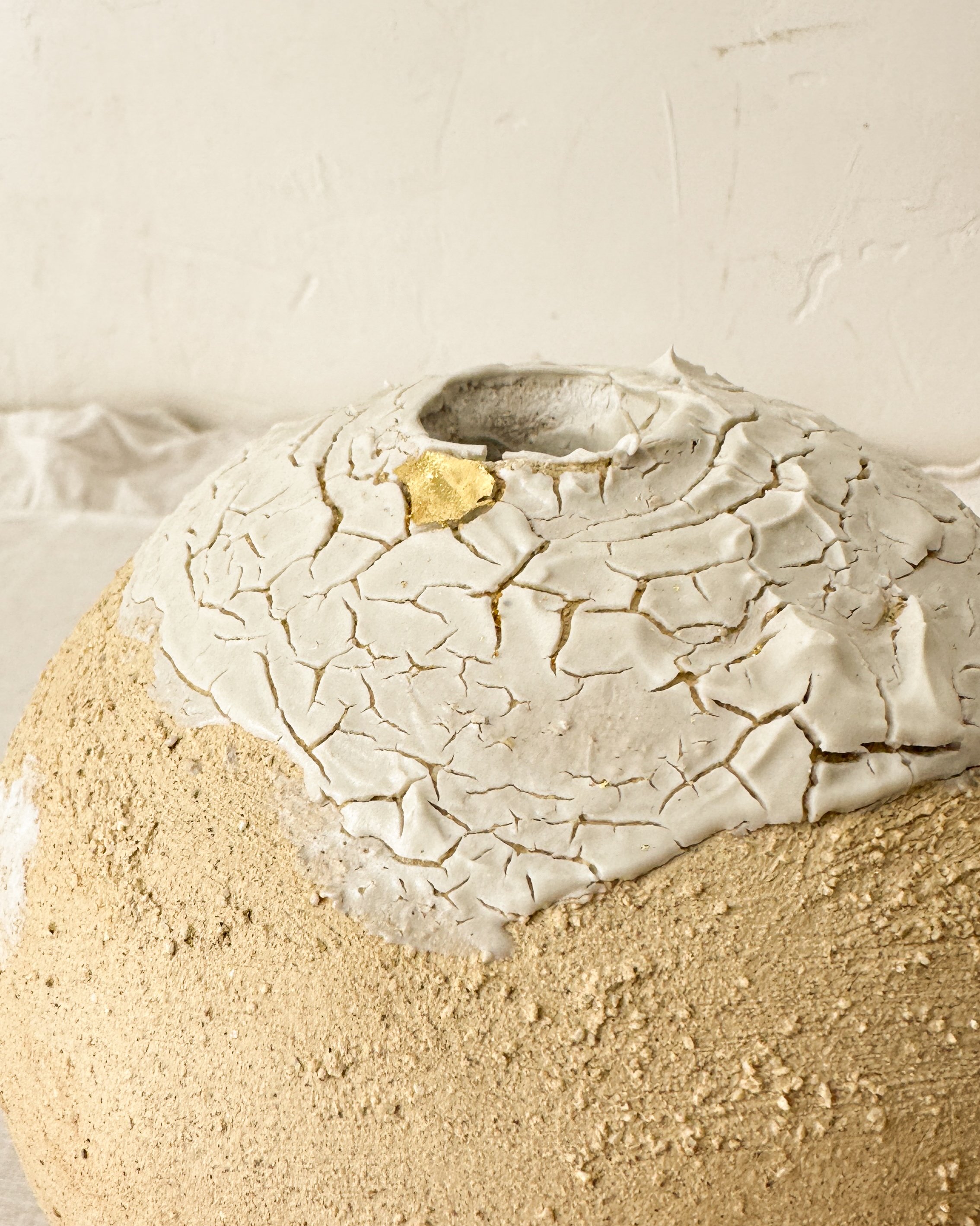 vase en argile sable  craquelée posée dans un décor contemporain minimaliste , décorée avec un petit morceau d'or.