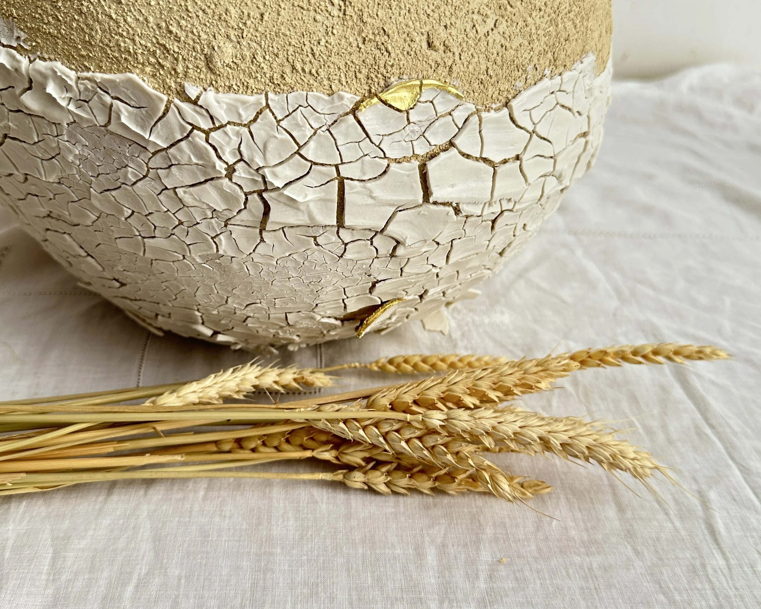 Un gâteau avec une couche de glaçage beige et décoré de blé et d'une bande de gâteau blanc avec un motif de fissures. Le gâteau est placé sur une surface beige, décorée de plusieurs tiges de blé.