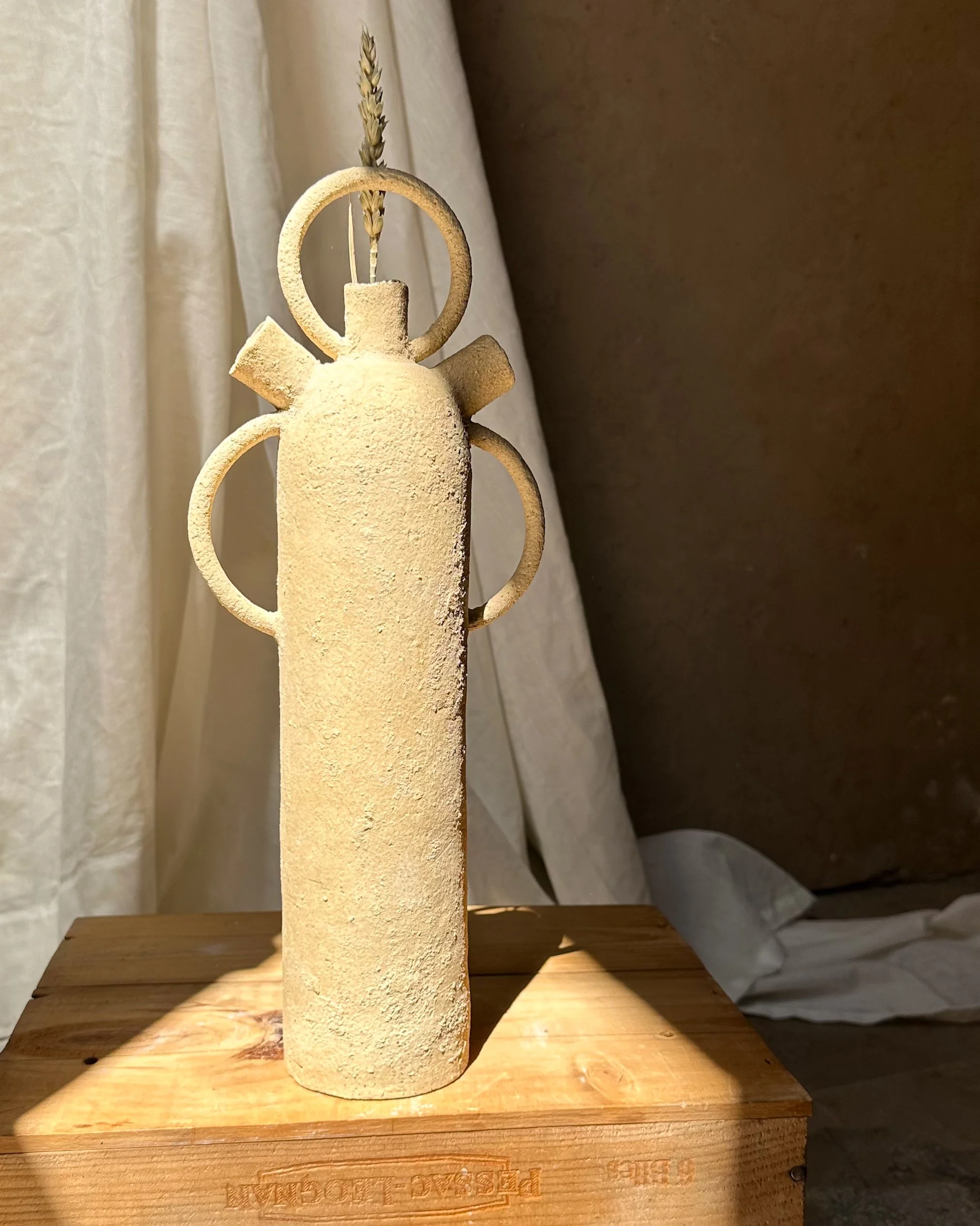 Une sculpture en forme de boule avec des cercles entourant l'objet, une bougie au centre, une tige avec du blé derrière, posée sur une surface en bois.