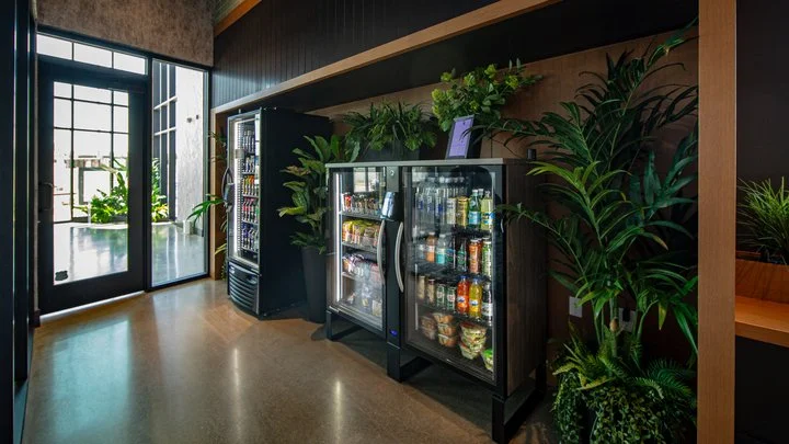 Indoor space with vending machines, potted plants, and large windows letting in natural light.