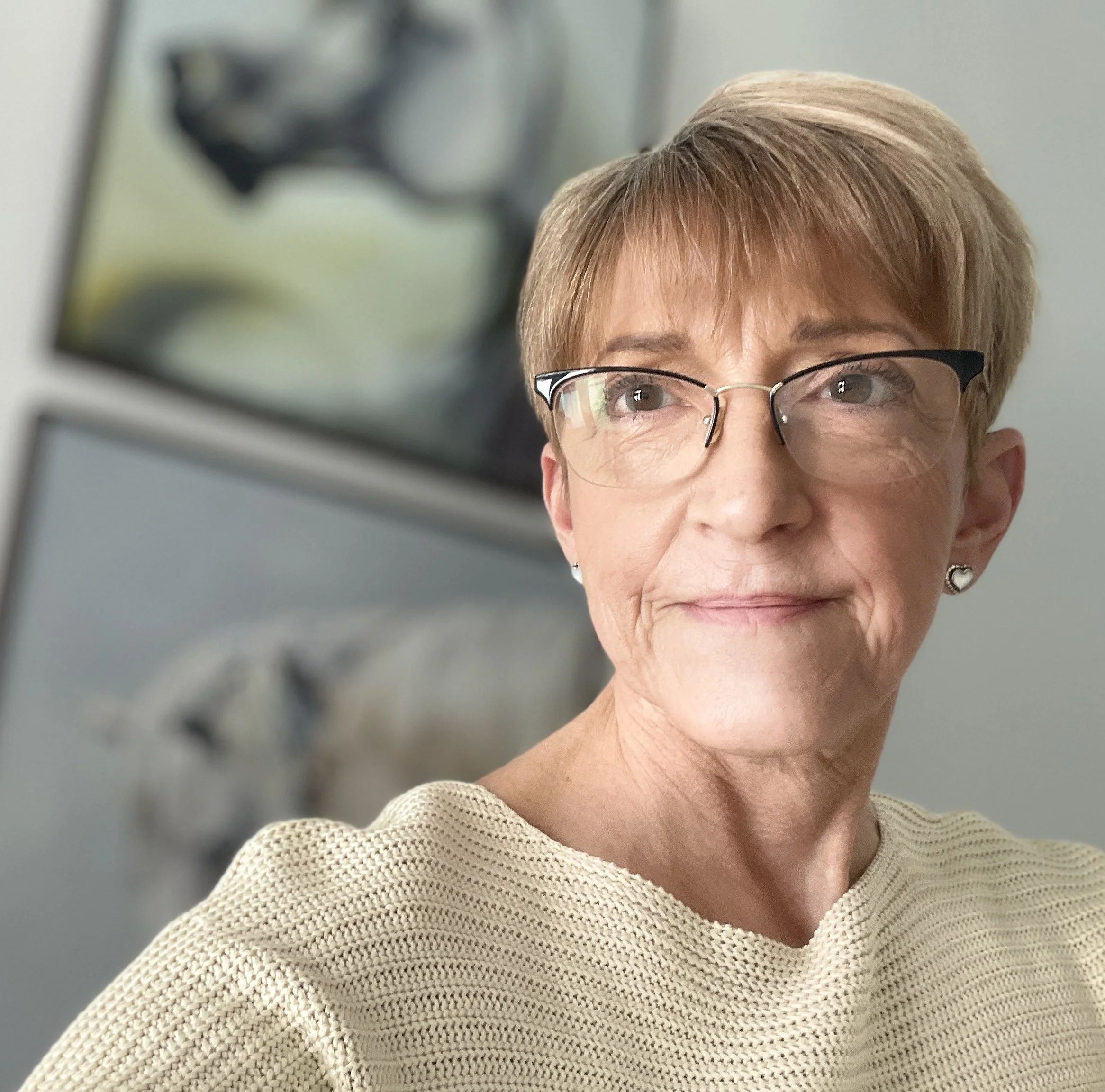 Close-up of a woman with short blonde hair, wearing glasses and a beige knitted sweater.