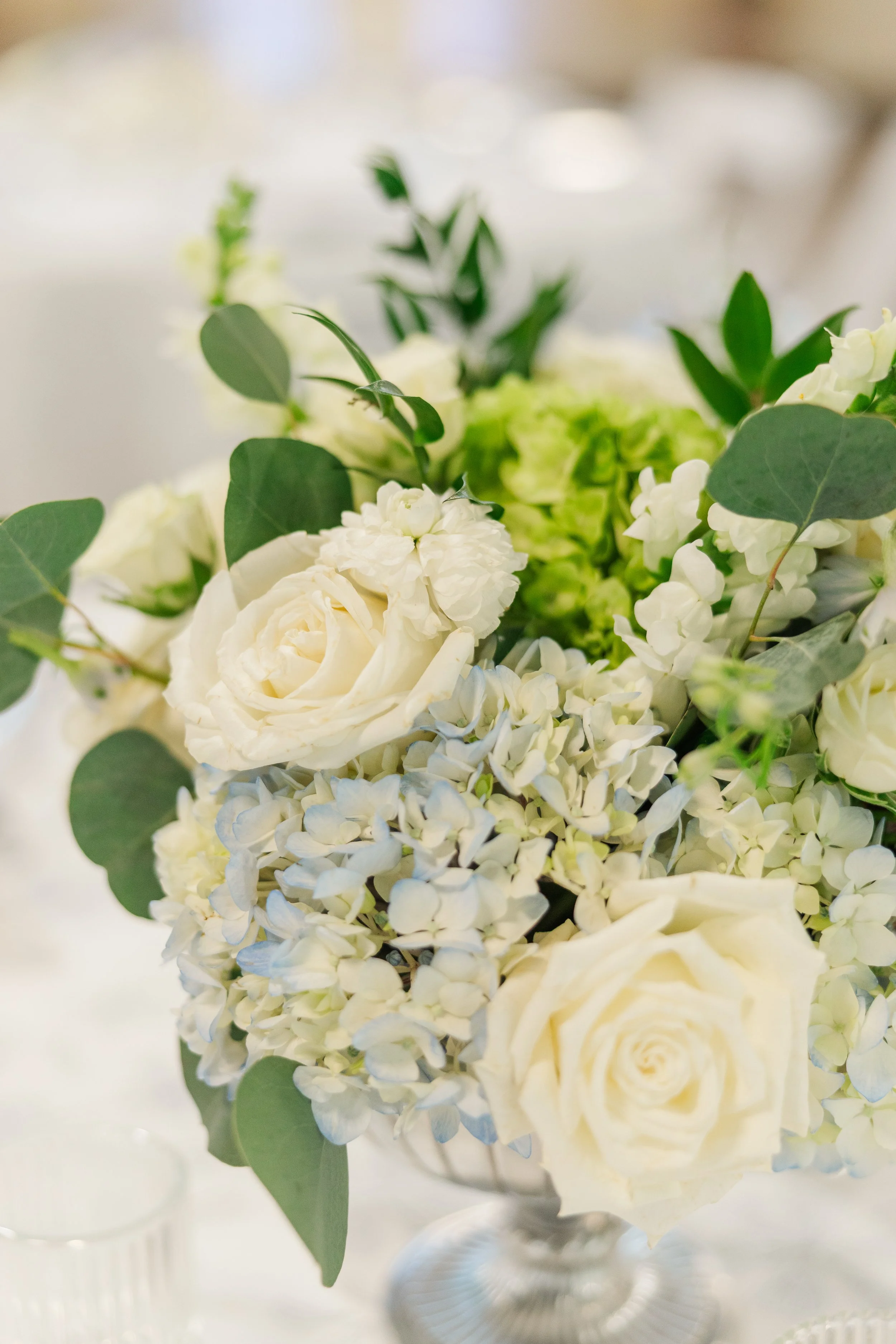 White roses, hydrangeas, and eucalyptus arranged in an elegant wedding centerpiece during the reception.