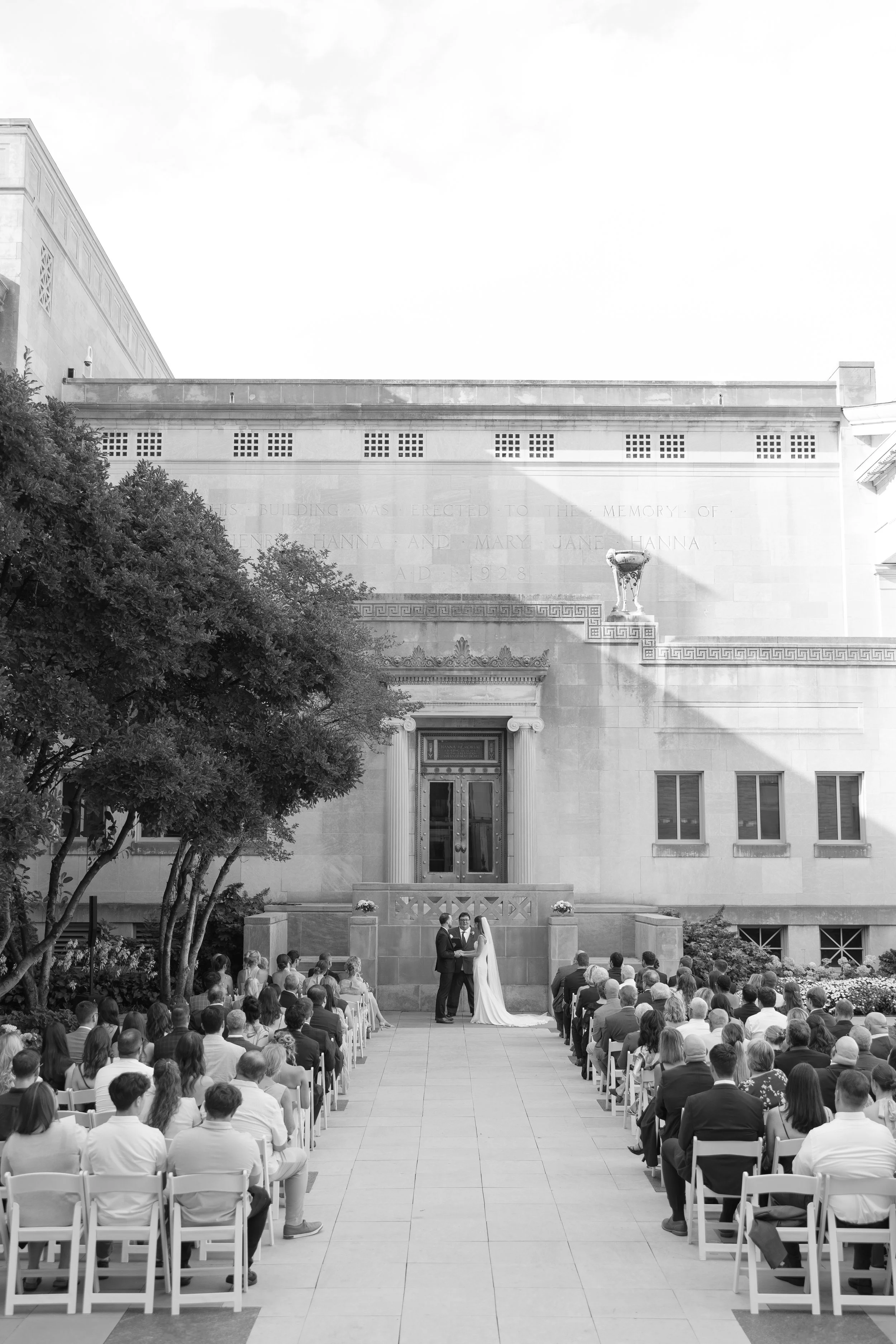 Bride and groom exchanging vows during an outdoor wedding ceremony with guests in attendance at The Cincinnati Art Museum. 