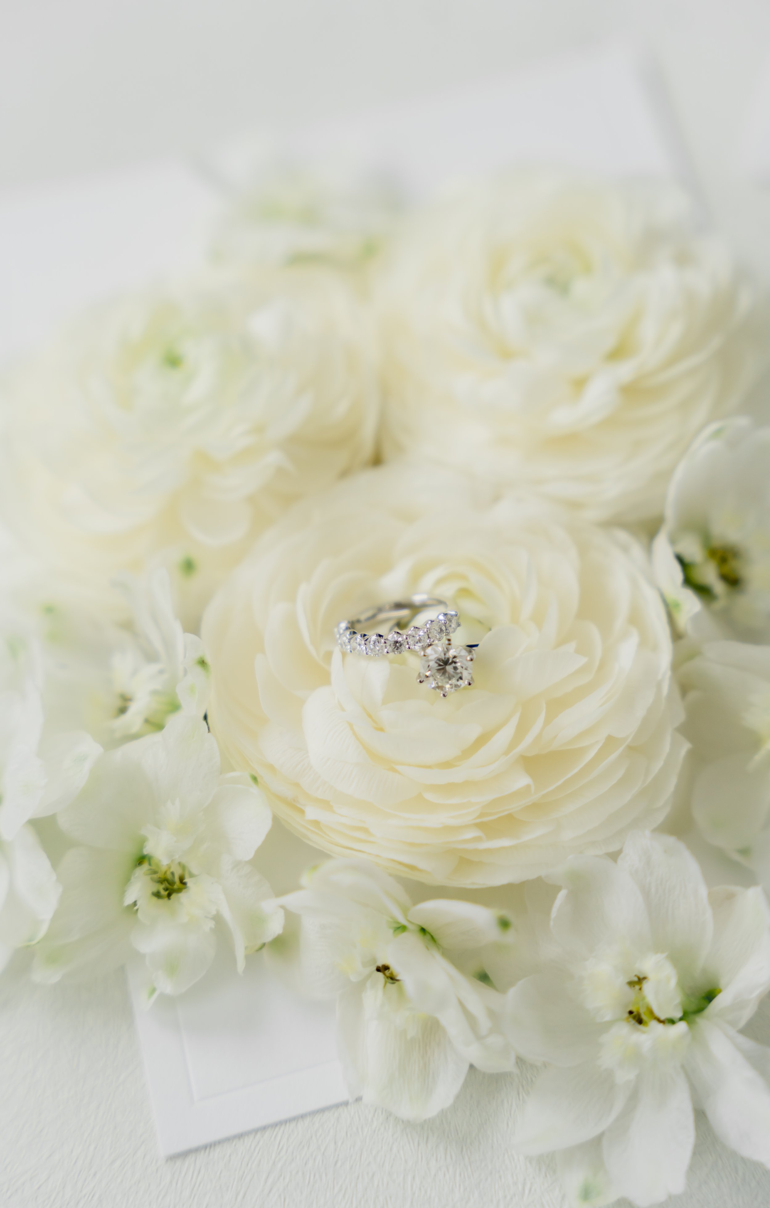 Close-up of a bride’s diamond engagement ring resting on white ranunculus flowers during a Cincinnati wedding planned by Leeann McKay Events.