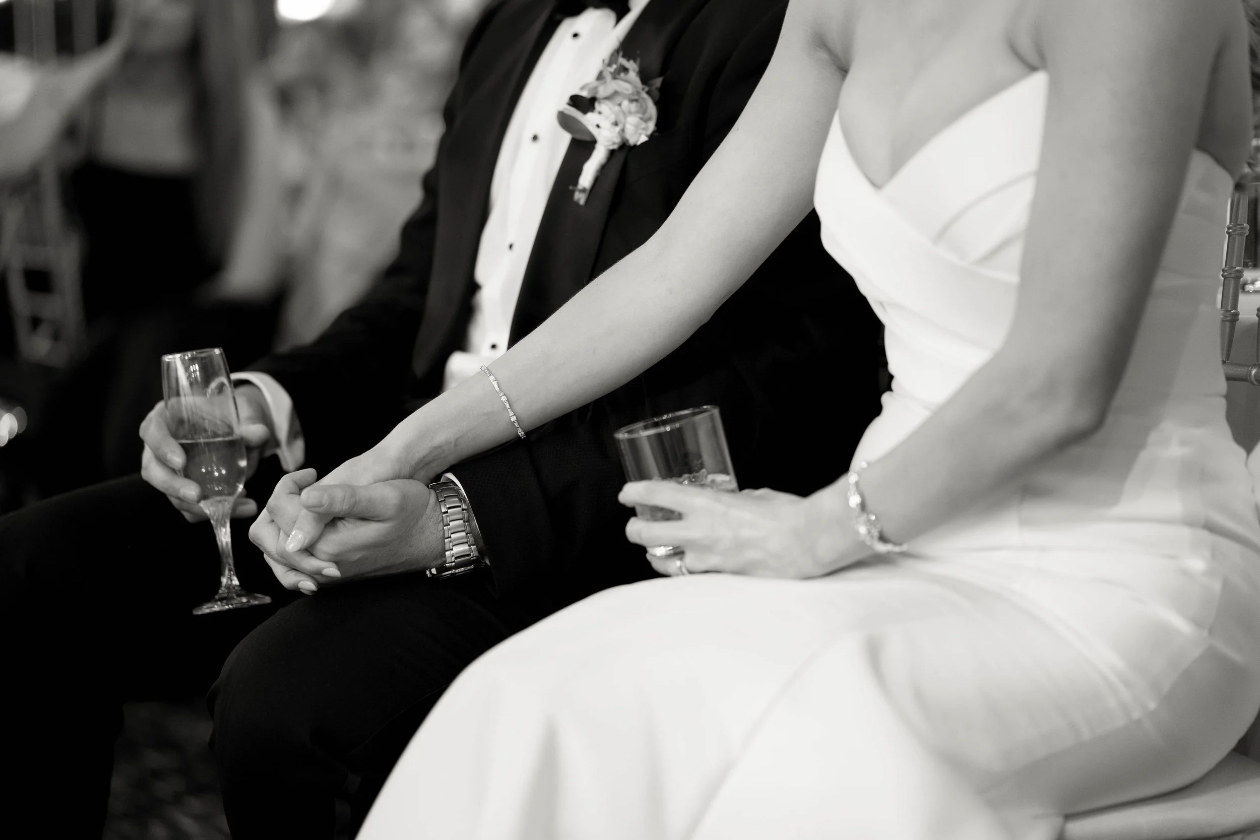 People sitting side by side at a formal event, holding glasses, dressed in elegant attire, black and white photo.