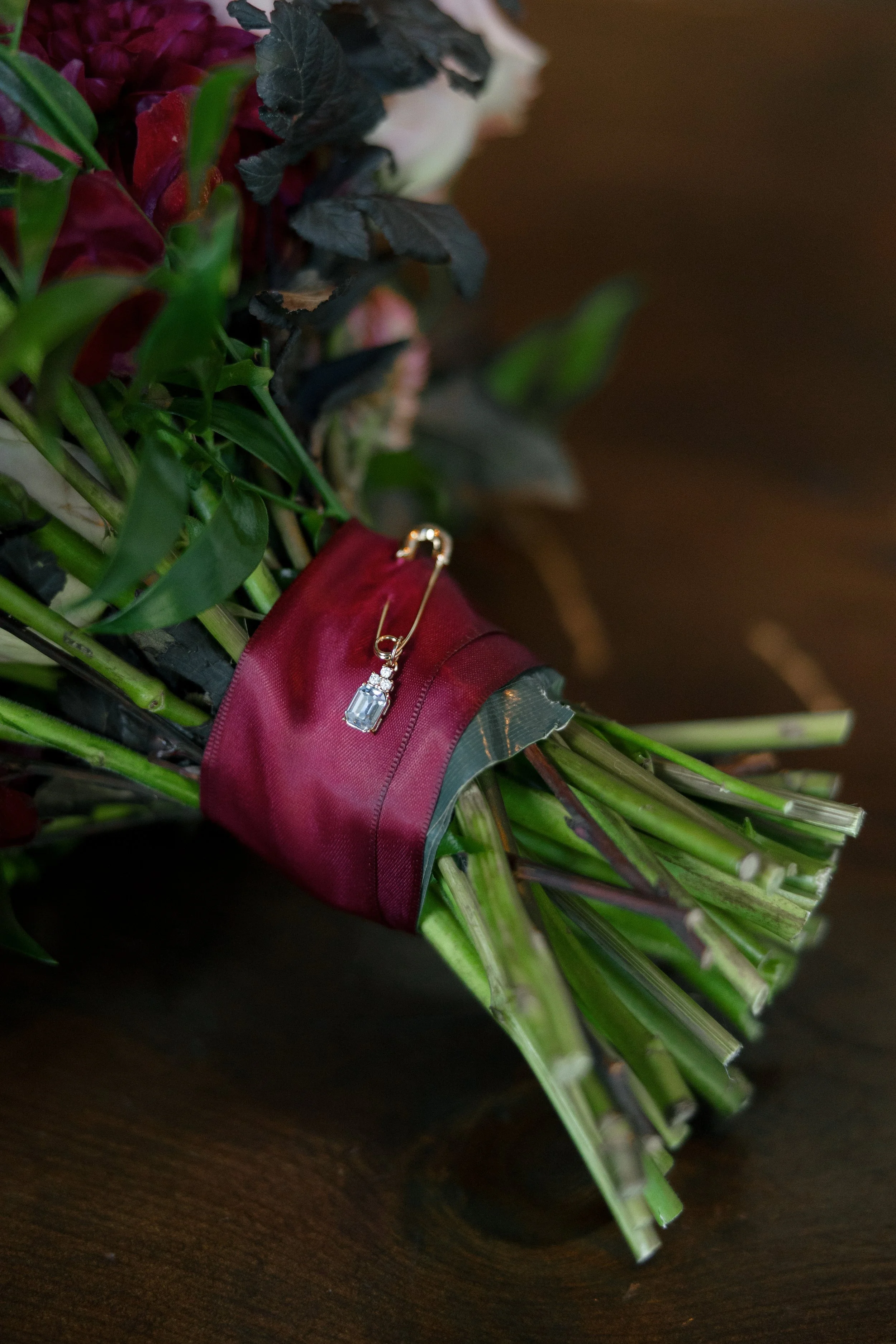 Wedding day detail featuring an heirloom pin on a bridal bouquet with burgundy ribbon.