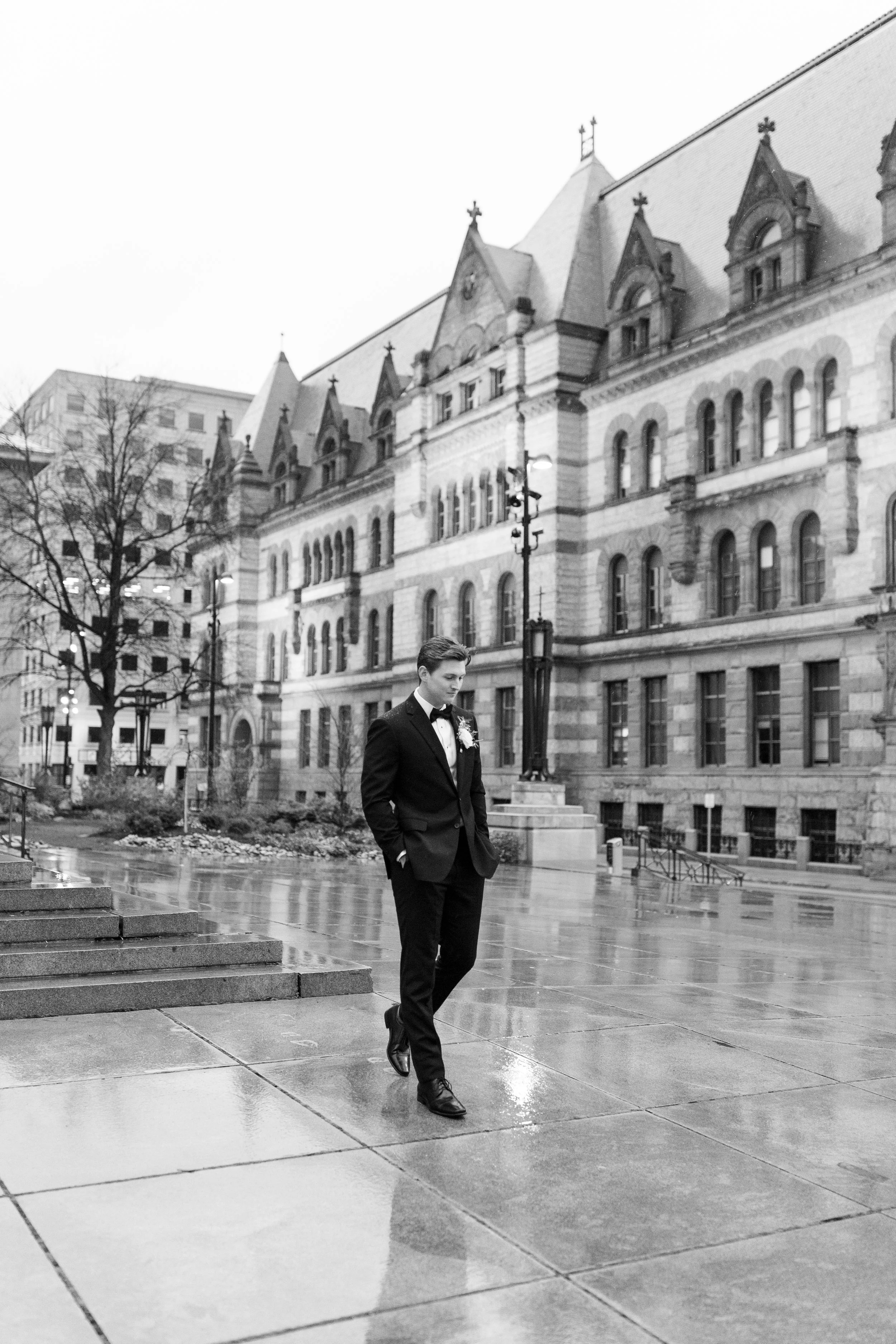 Groom in a classic black tuxedo posing outside the Cincinnati Club on a rainy wedding day.