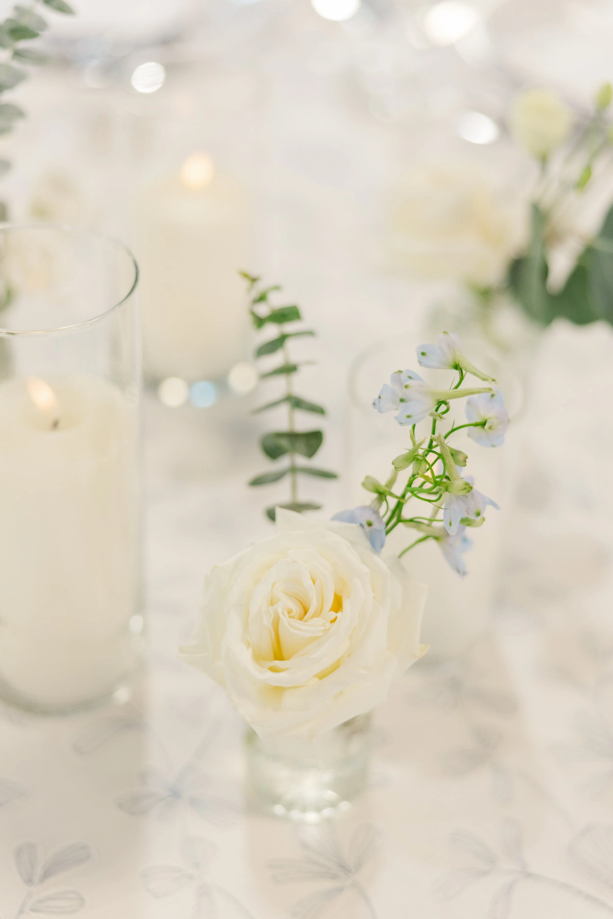 Elegant white rose bud vase centerpiece displayed on a candlelit wedding reception table.