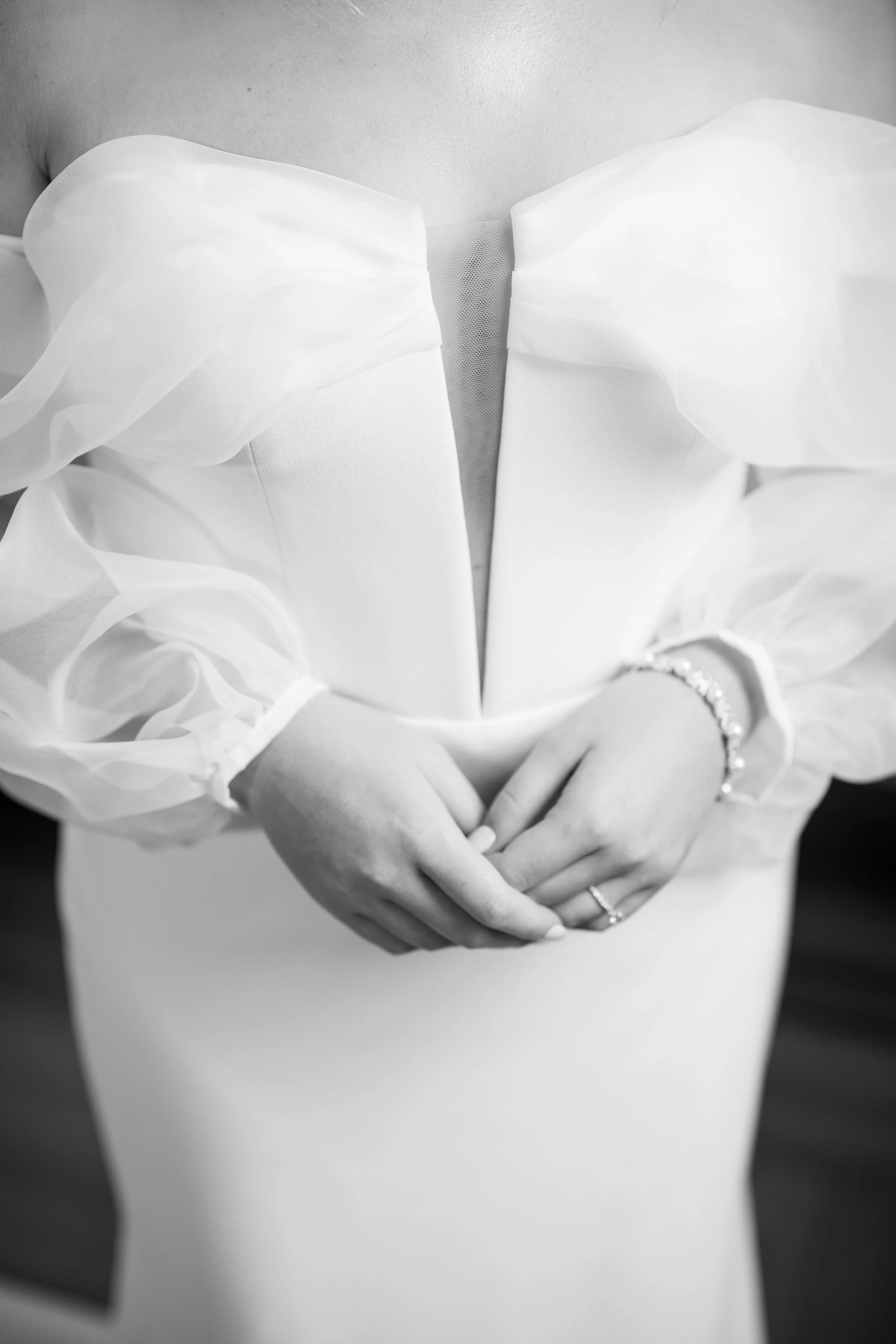 Close-up of the bride’s hands resting on the front of her elegant satin wedding gown, highlighting timeless bridal details.