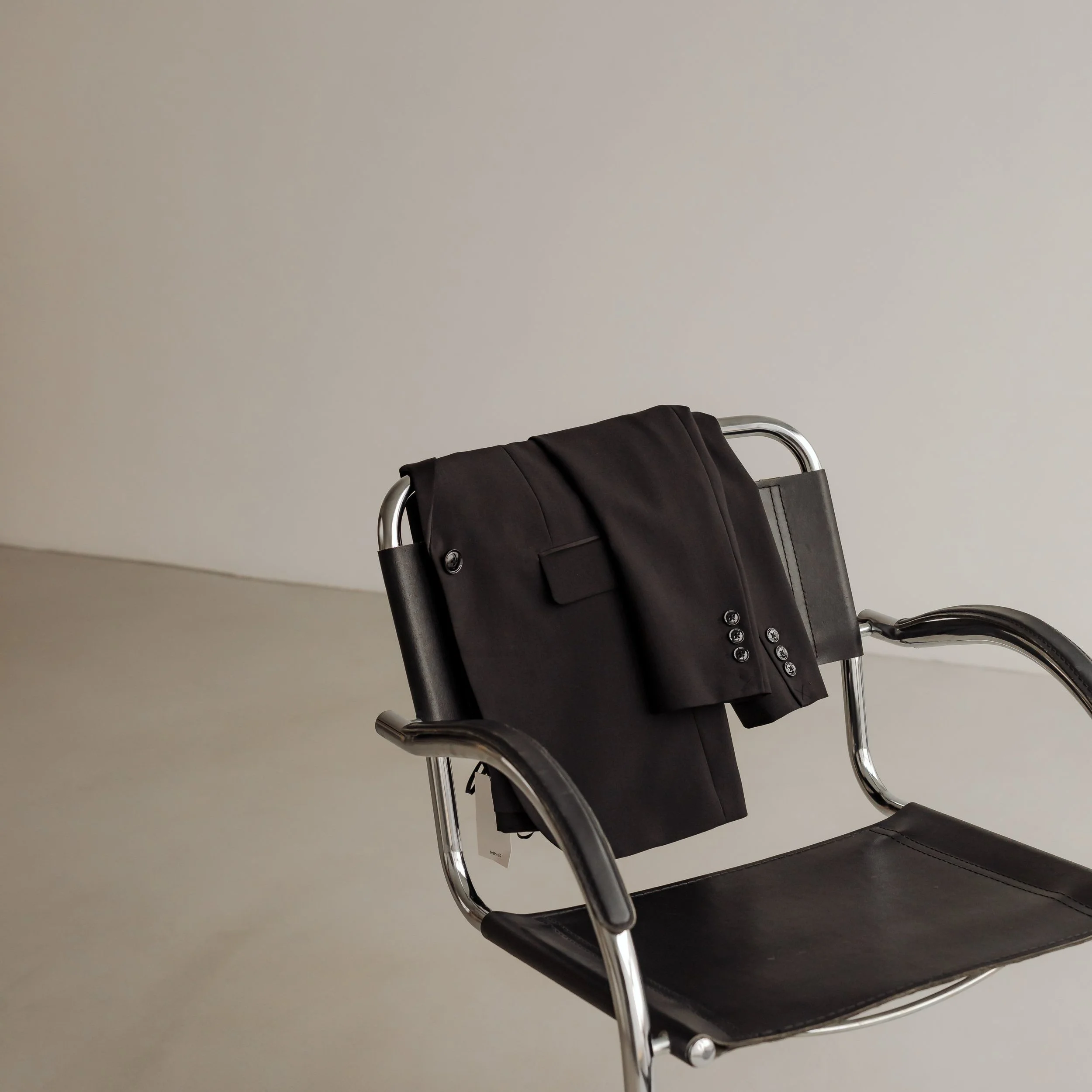 Empty black wheelchair with metal frame and black cushion seat against a plain white wall.