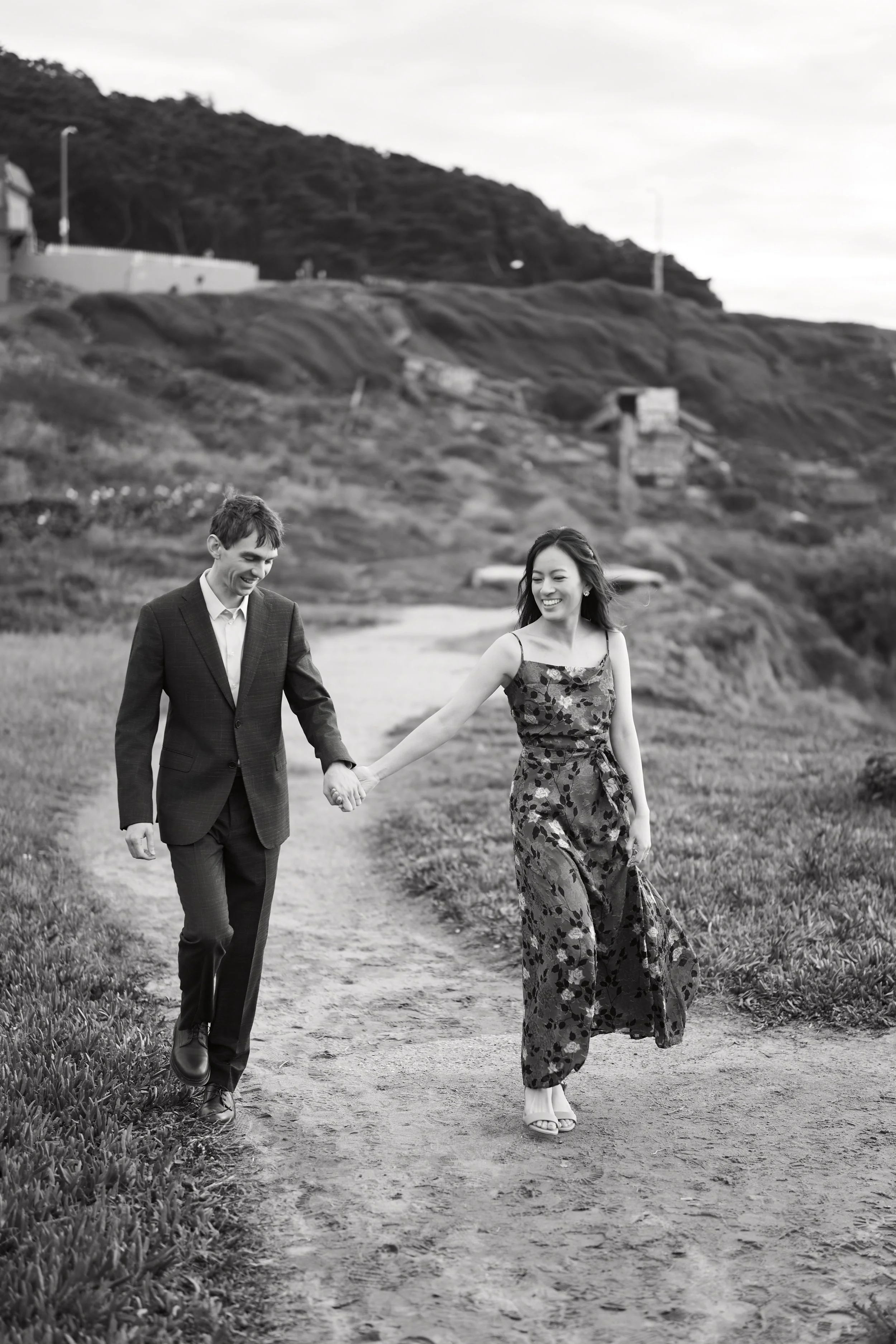 Black and white candid of a couple walking the Lands End path, laughing
