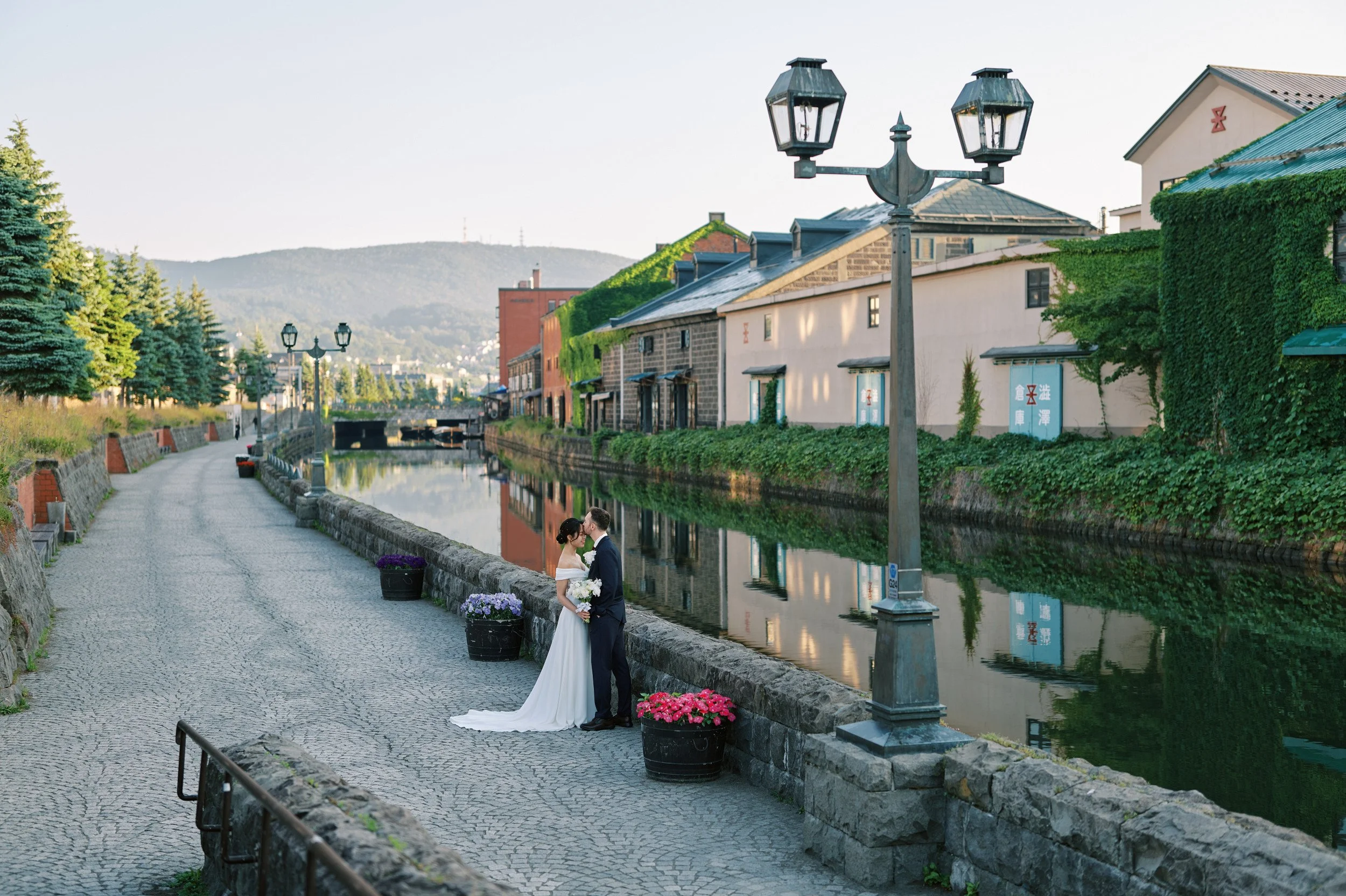 Wide view of the Otaru Canal at dawn with the couple beneath a vintage gas lamp