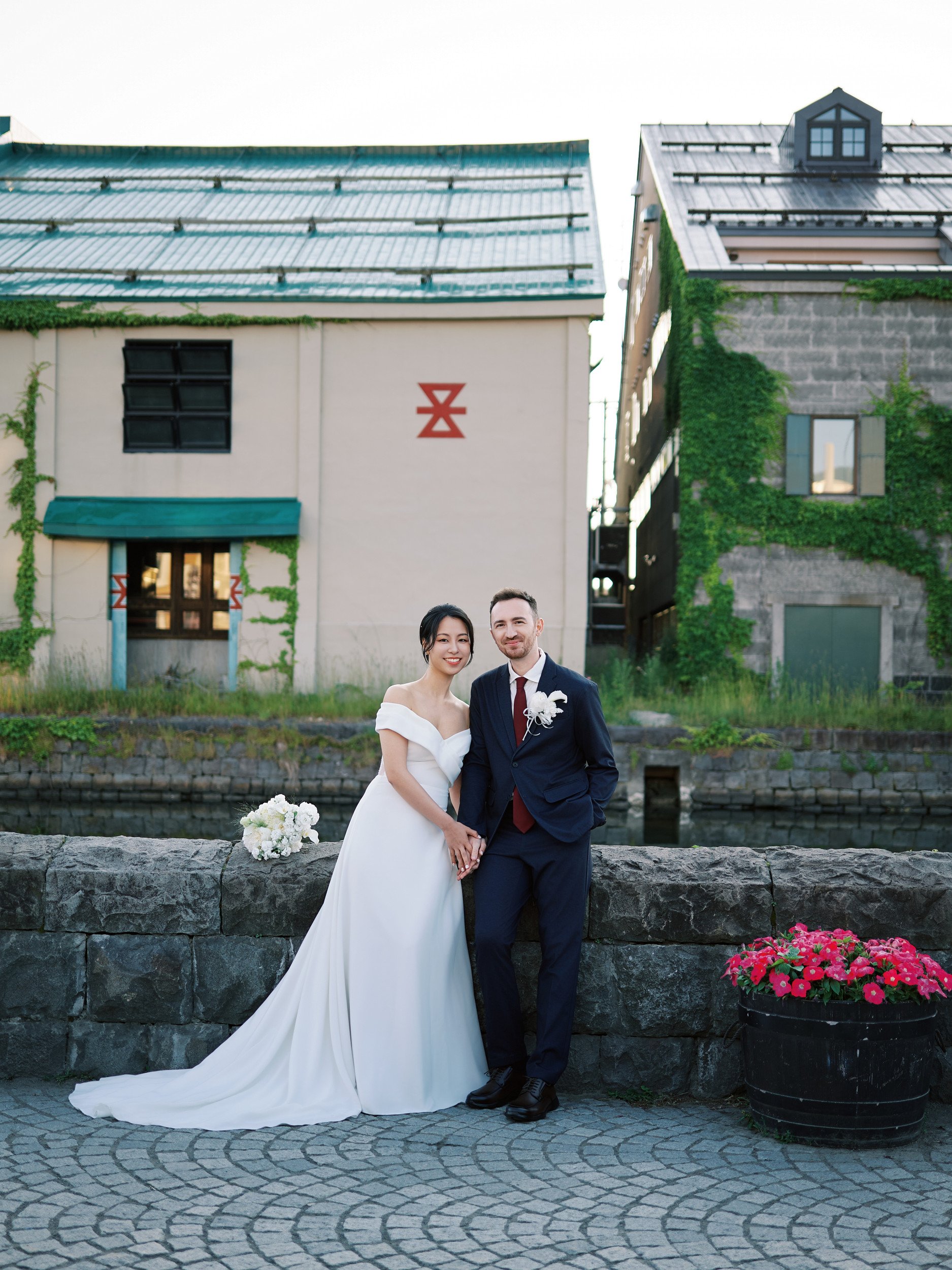 Couple holding hands by the canal railing as first light reaches the ivy-covered warehouses of Otaru
