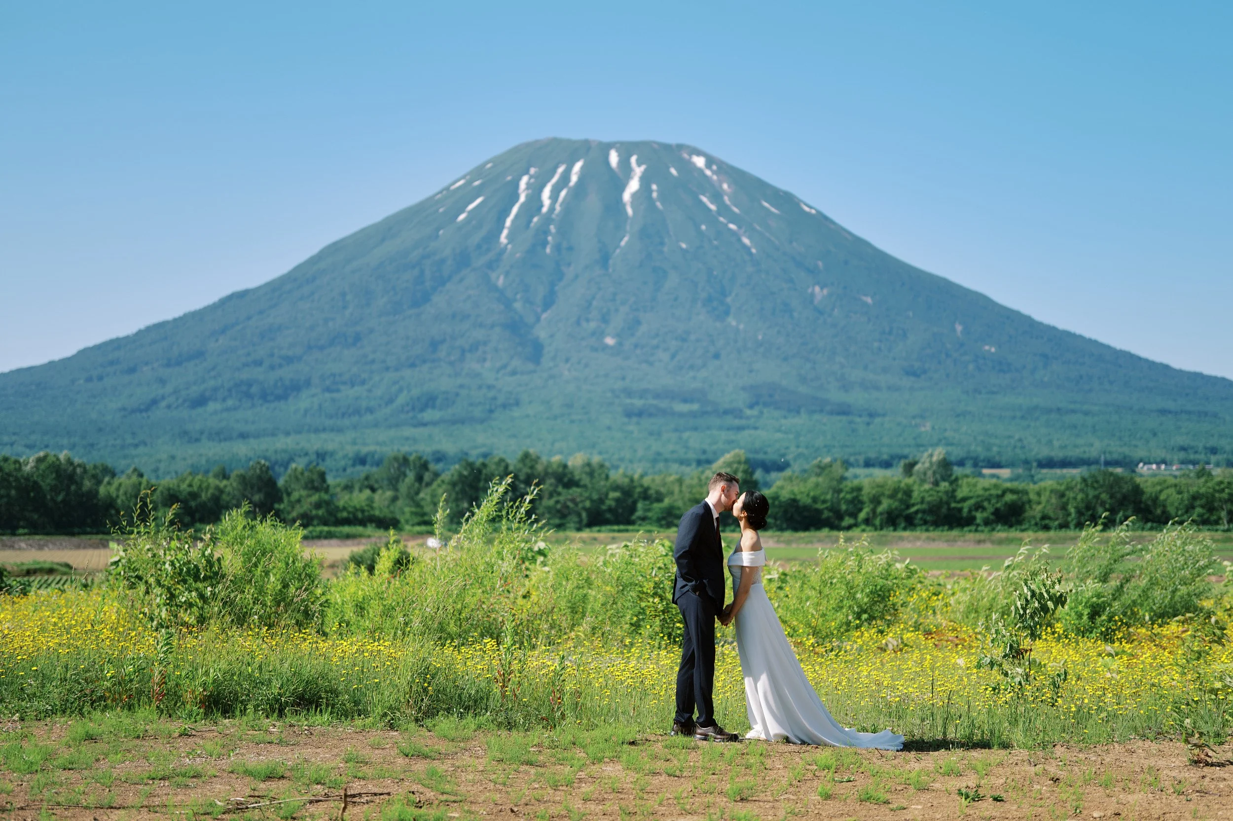 Couple standing in a green field beneath Mt. Yotei during their Hokkaido pre-wedding session in June