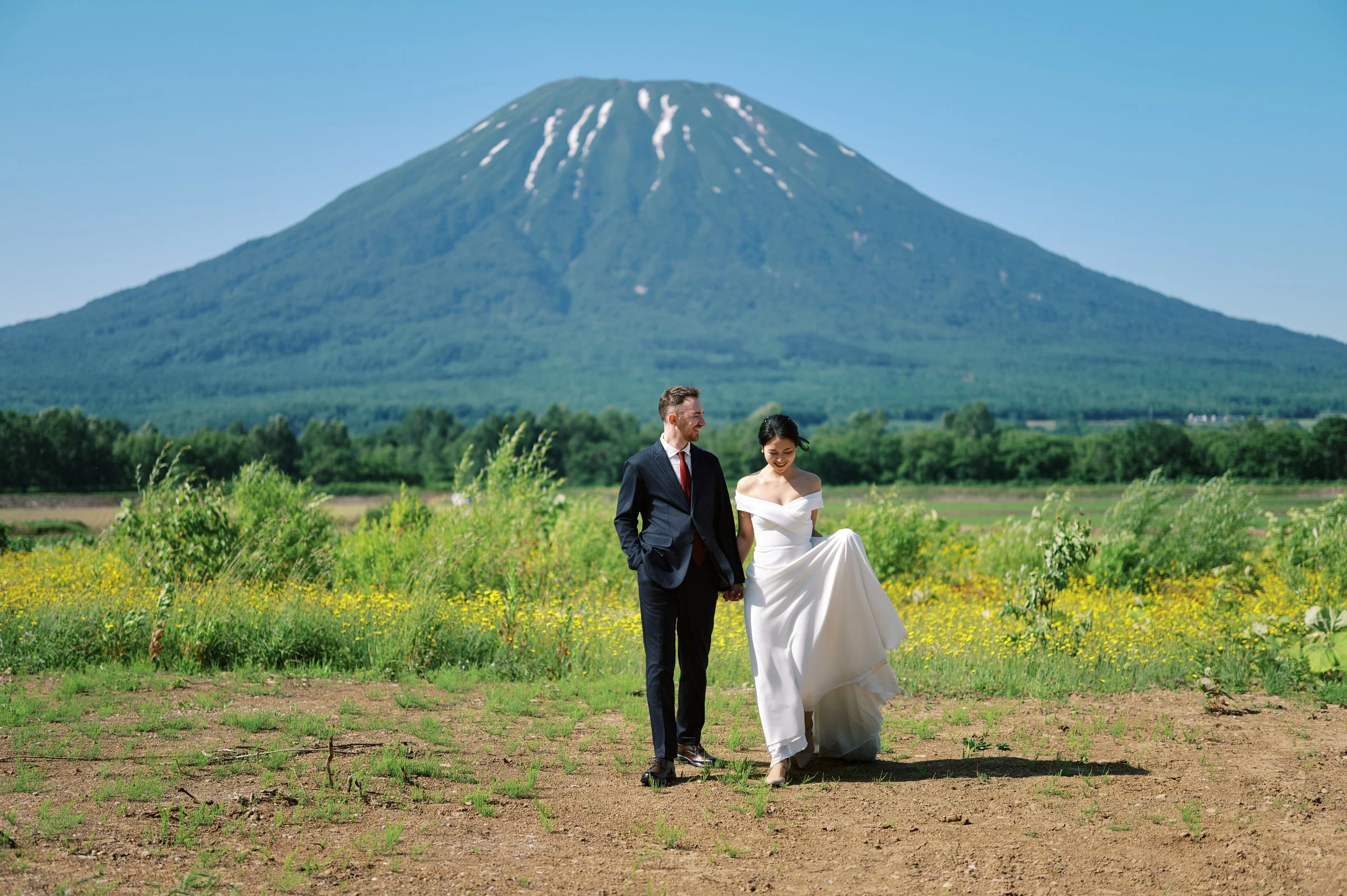 Bride and groom embracing with the full cone of Mt. Yotei rising behind them