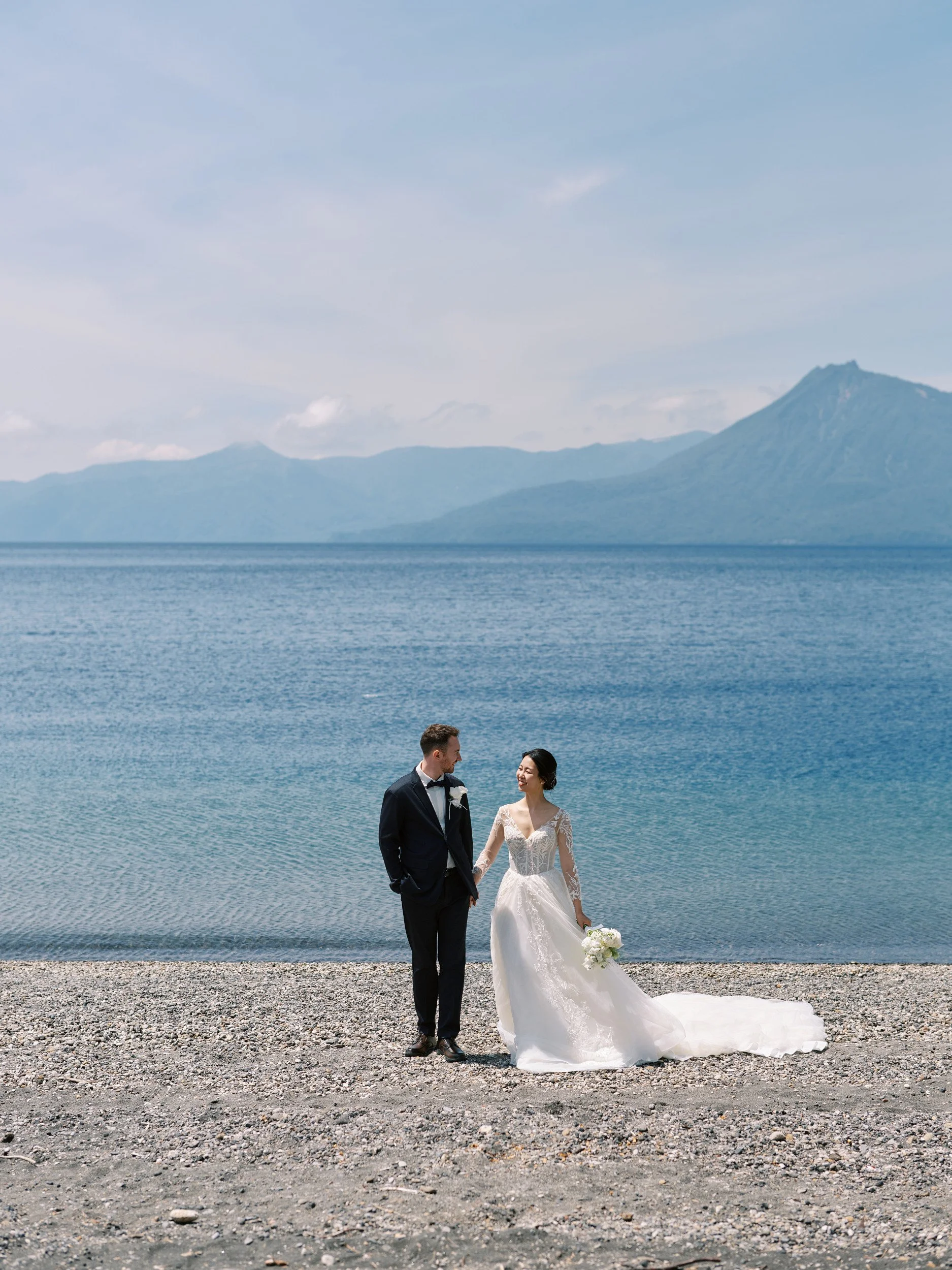 Bride and groom walking the pebbled shore of Lake Shikotsu hand in hand