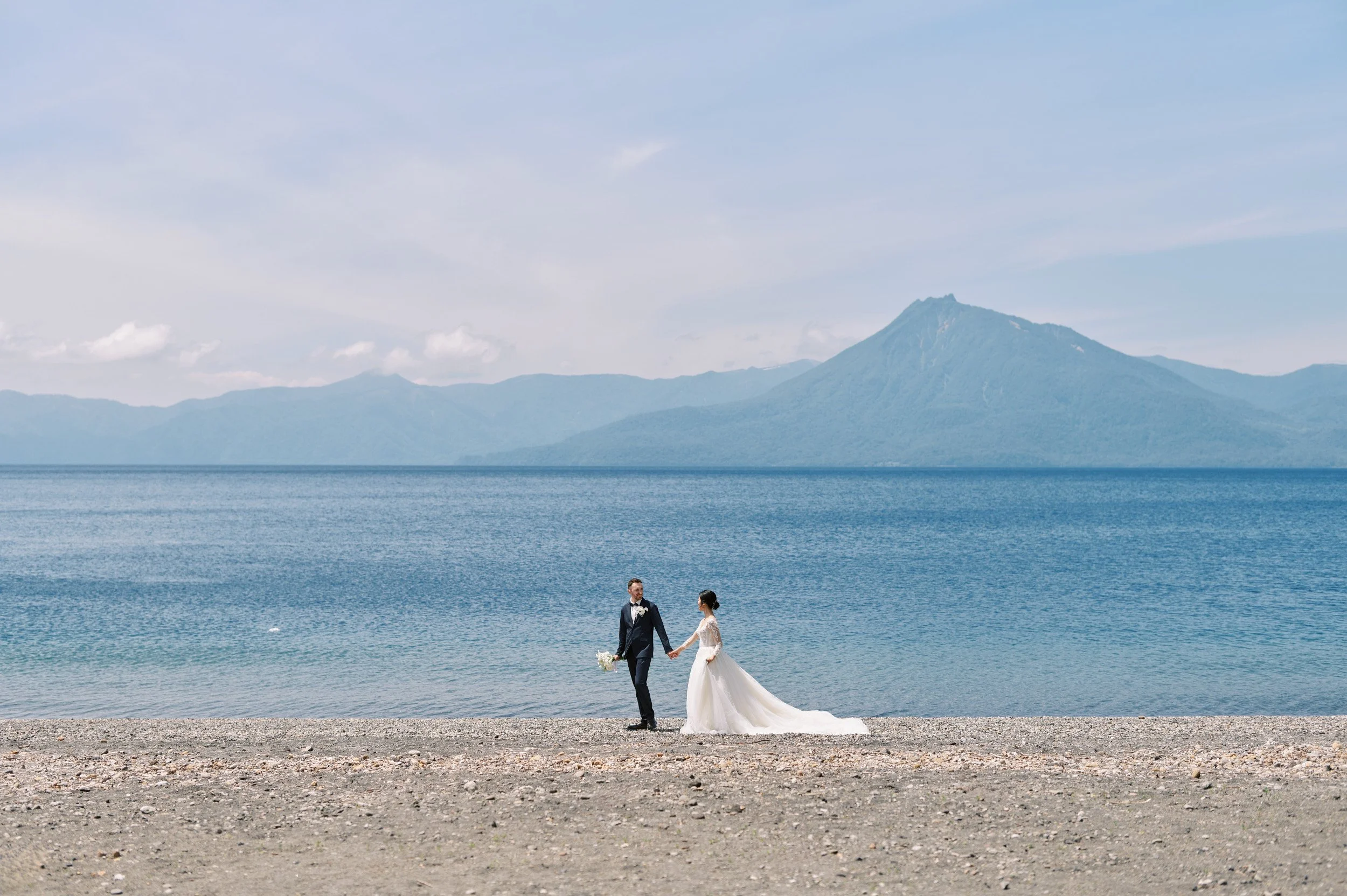 Couple at the edge of Lake Shikotsu with clear blue water and forested hills behind
