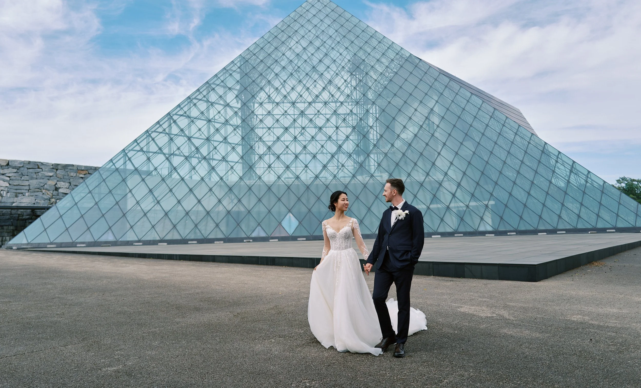 Bride and groom framed by the geometric glass architecture of Moerenuma Park