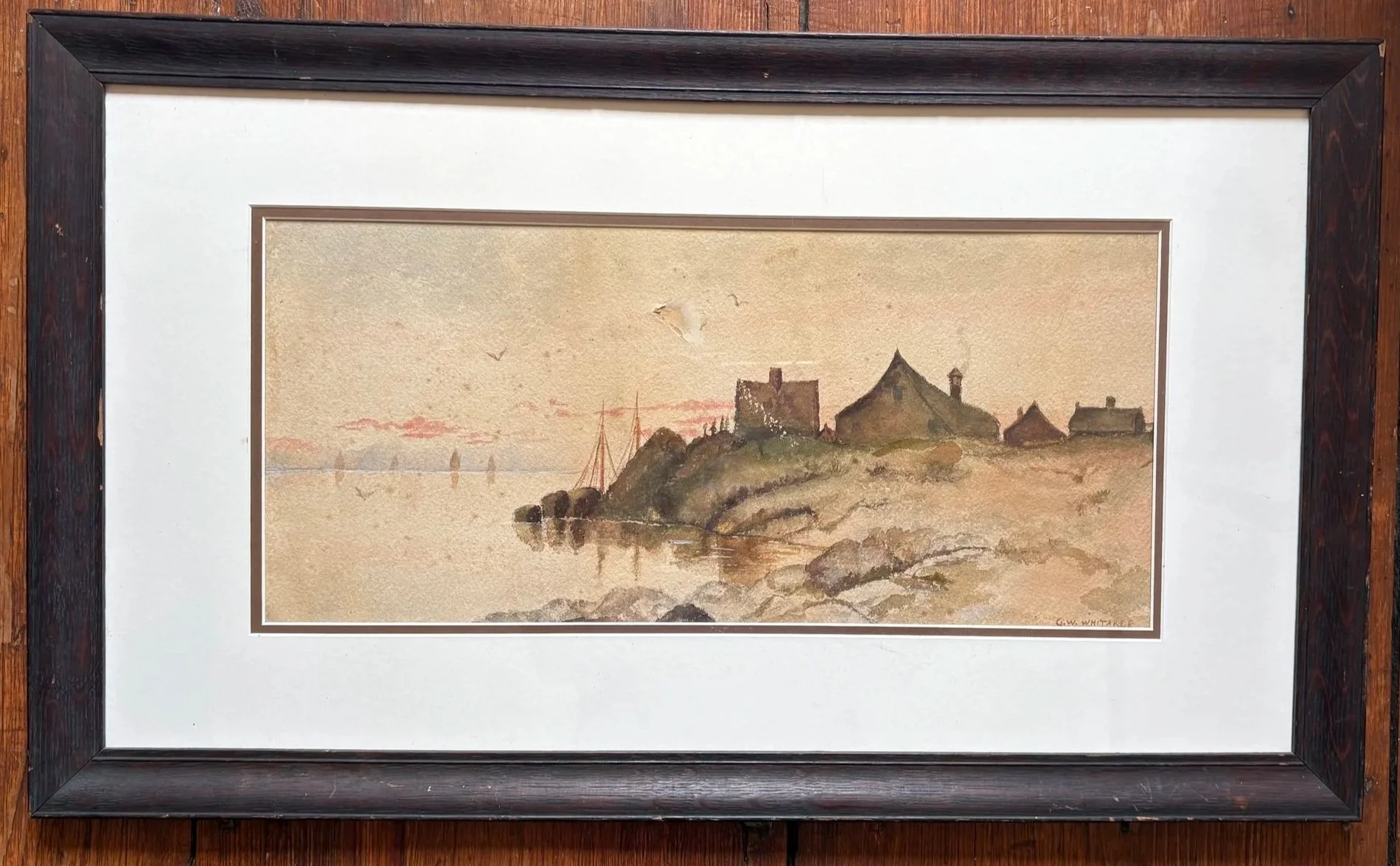 Watercolor painting of a coastal scene with a hilltop castle, smaller buildings, sailboats on the water, and birds flying in the sky, signed 'G.W. Whitaker'.