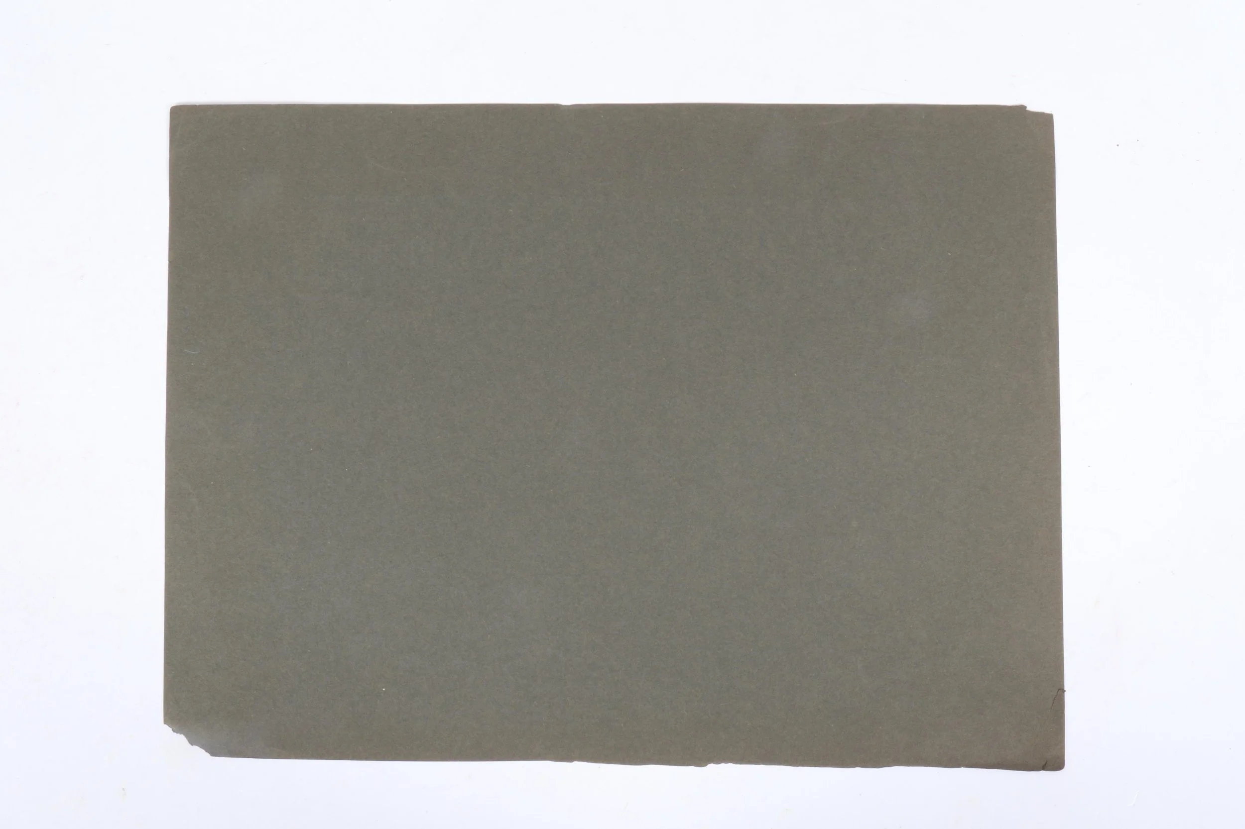 A sheet of grey paper with slightly torn edges placed on a white surface.