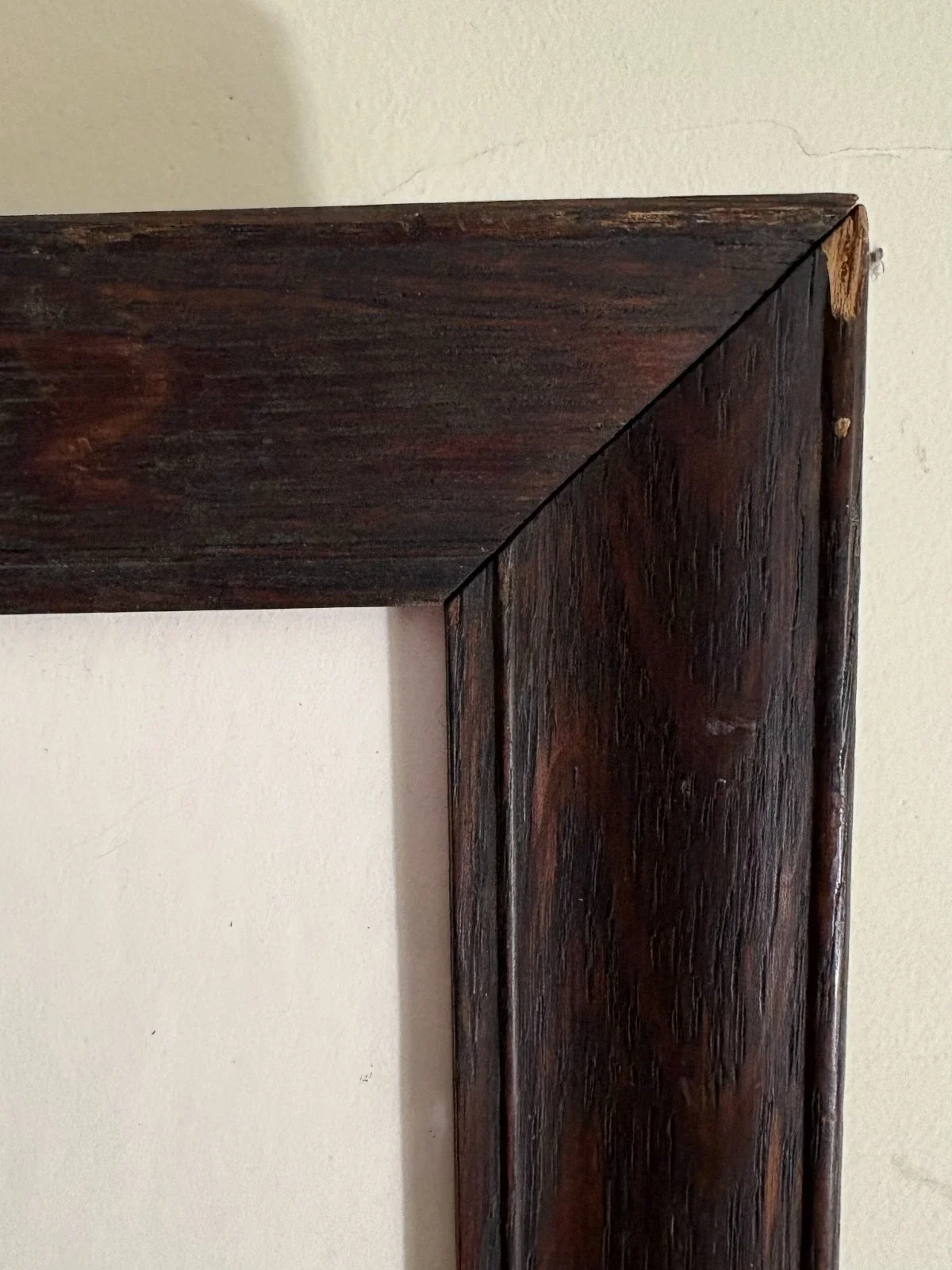Close-up of a wooden picture frame corner against a white wall.