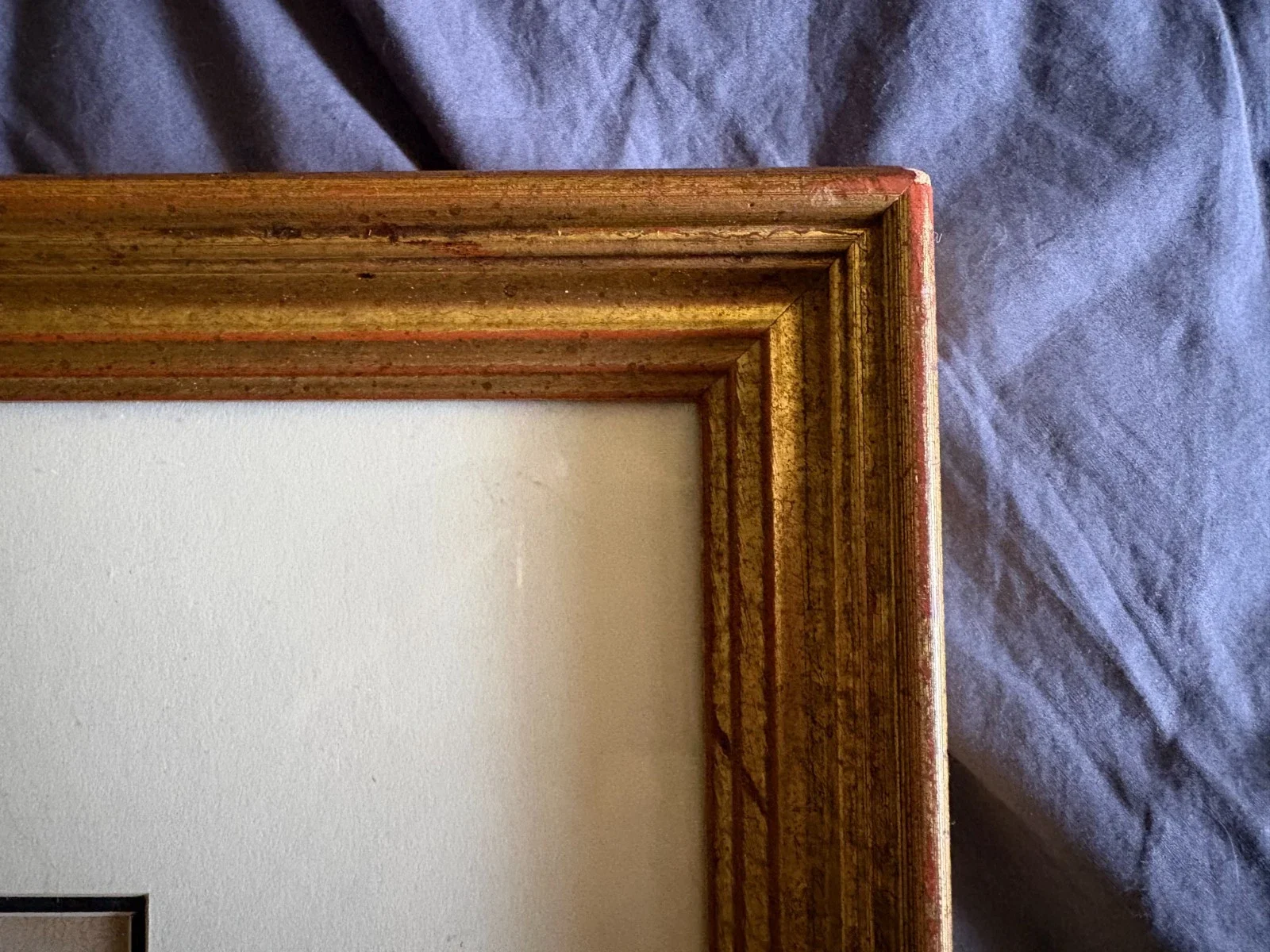 Close-up of a gold wooden picture frame corner resting on a purple fabric surface.