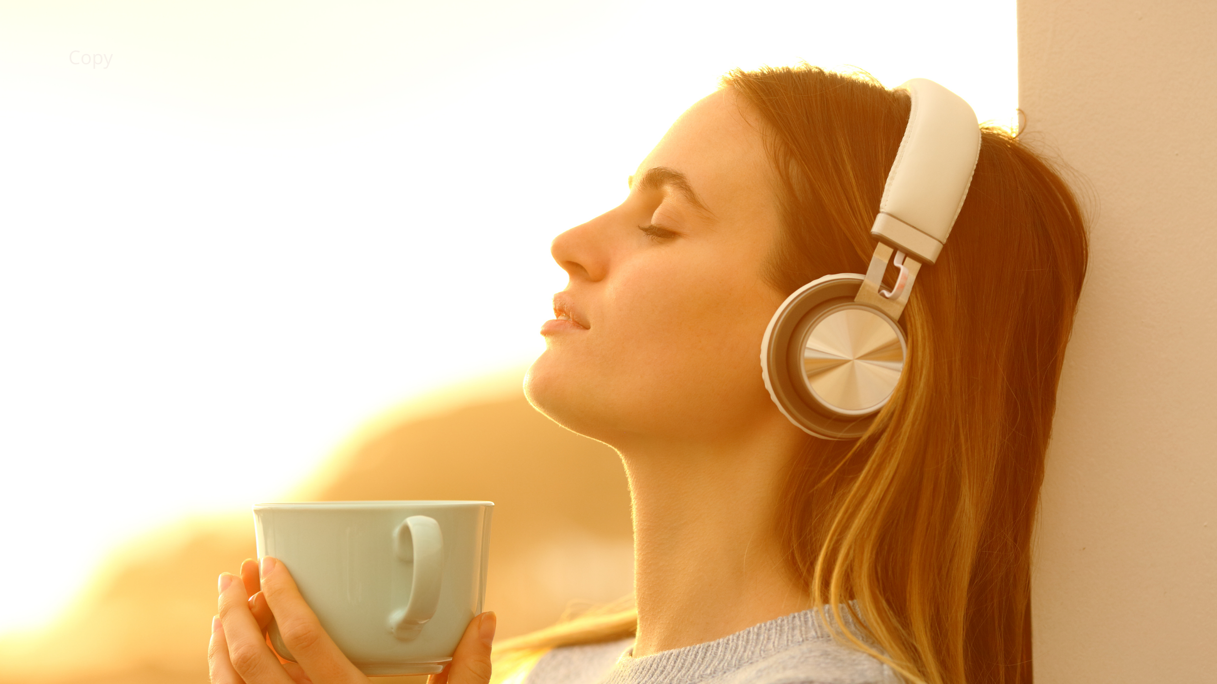 A woman with red hair wearing white headphones, holding a white mug close to her face, with her eyes closed, enjoying a peaceful moment during sunrise or sunset.