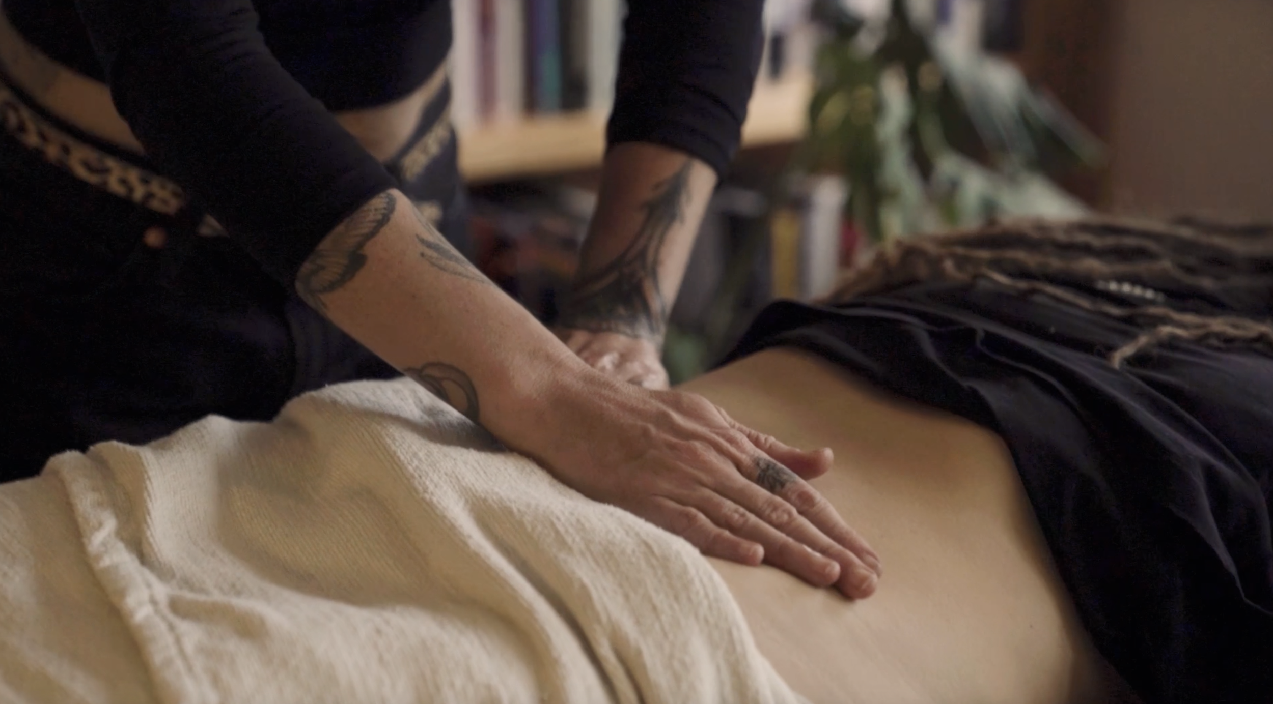 New mom receiving an Ayurvedic womb massage or stomach massage from Tania Marie while lying down on a massage table. Tania Marie's hands are applying pressure on the woman's belly.