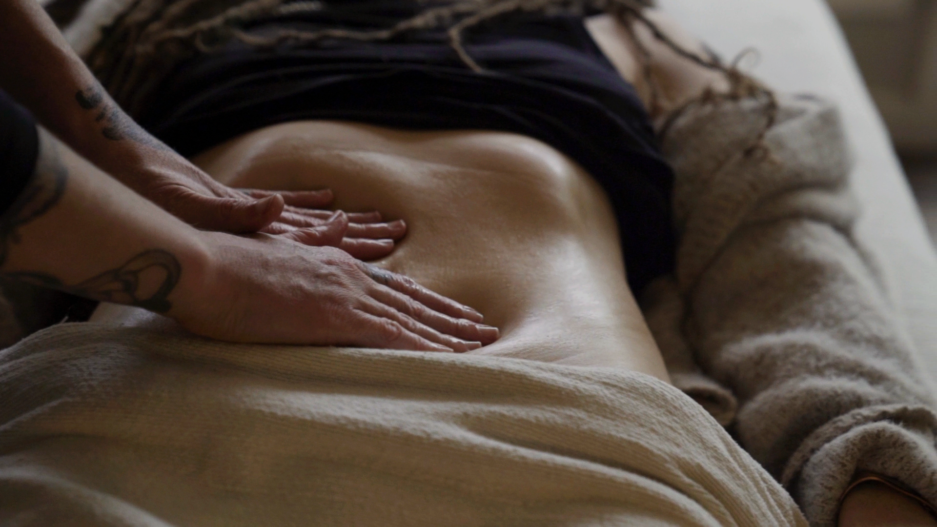 New mom receiving an Ayurvedic womb massage or stomach massage from Tania Marie while lying down on a massage table. Tania Marie's hands are applying pressure on the woman's belly.