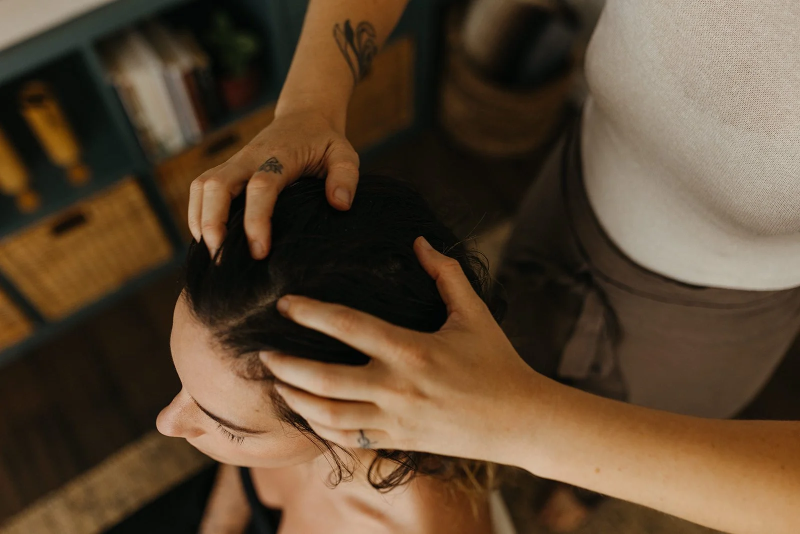 A person receiving a head massage or chiropractic adjustment, with hands on their head, in a cozy, home-like setting.