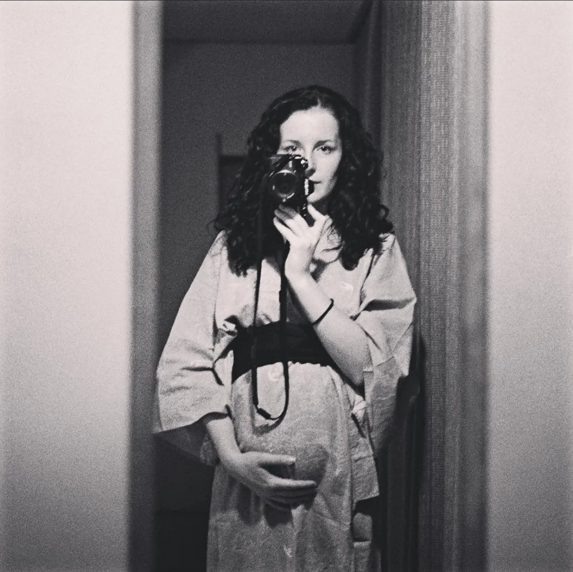 Black-and-white photo of Tania Marie, Tania Edwards, taking a mirror selfie with a camera, holding her pregnant belly, and wearing a Japanese kimono.