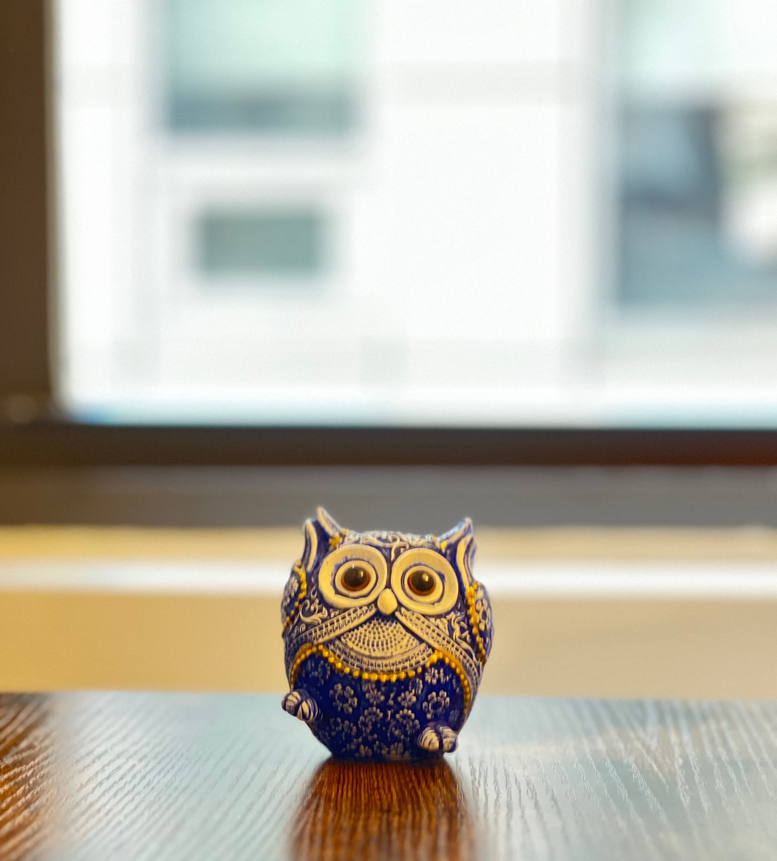 Colorful owl figurine with blue, yellow, and white decorative patterns, standing on a wooden surface.