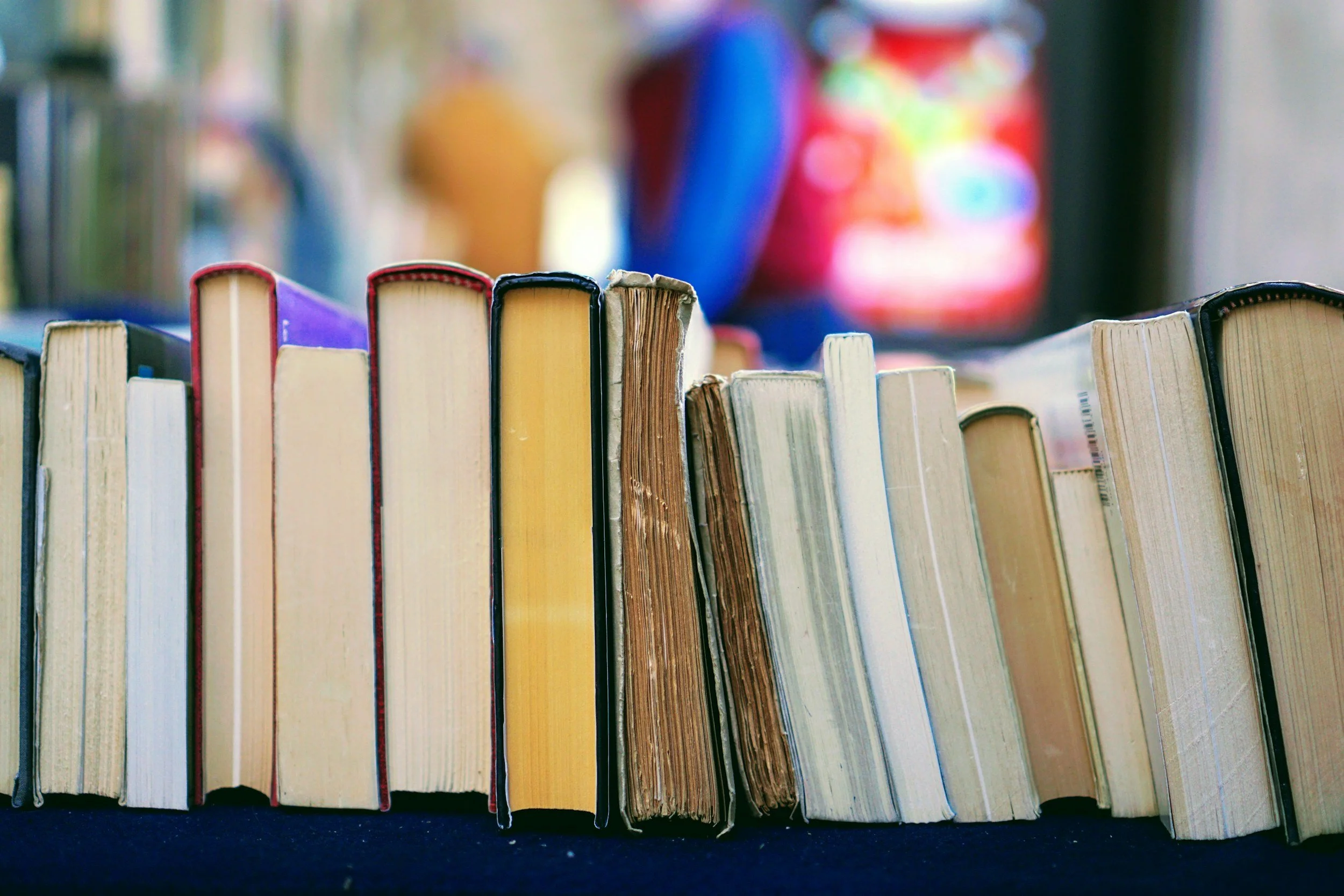 A row of used books with worn covers and pages, standing upright on a dark surface.