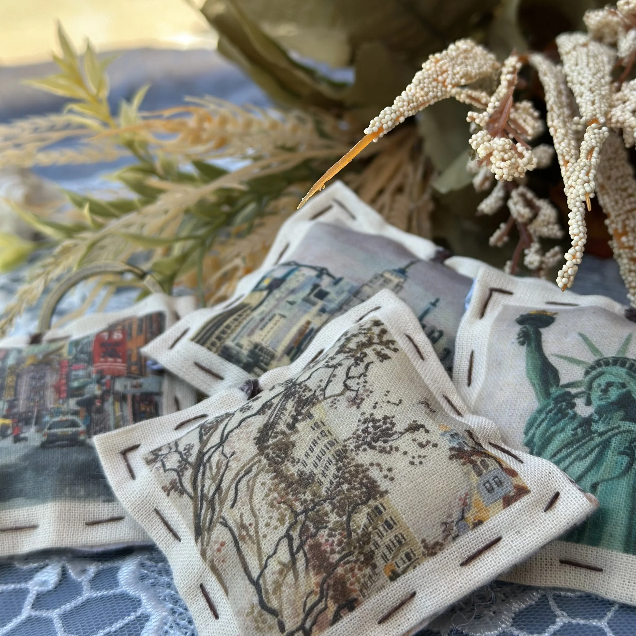 Close-up of a beaded art piece with intricate patterns and script on fabric, surrounded by decorative dried flora and leaves, displayed on a textured surface.