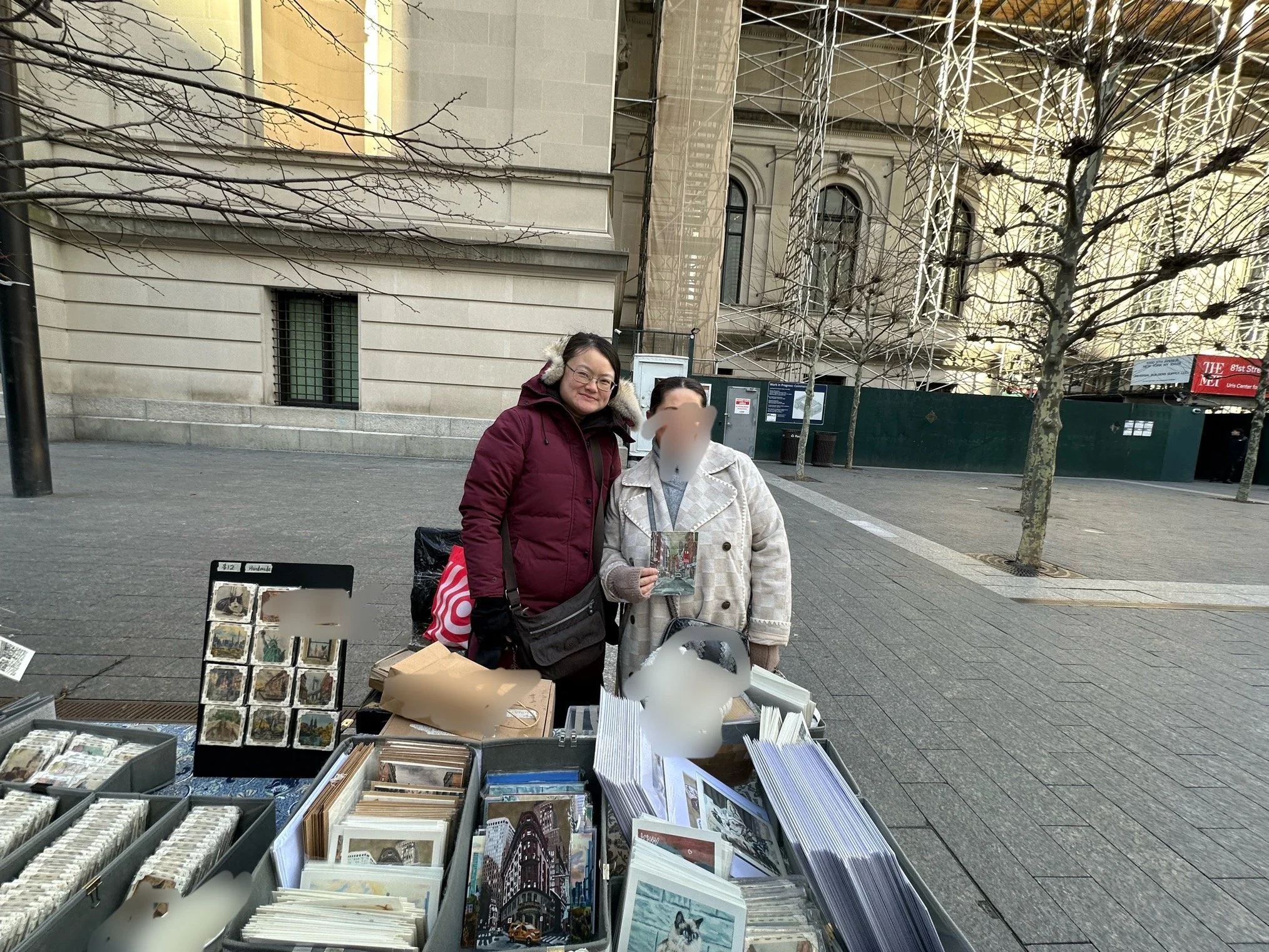 Two women standing behind a table displaying original work of Chinatown outside of The MET