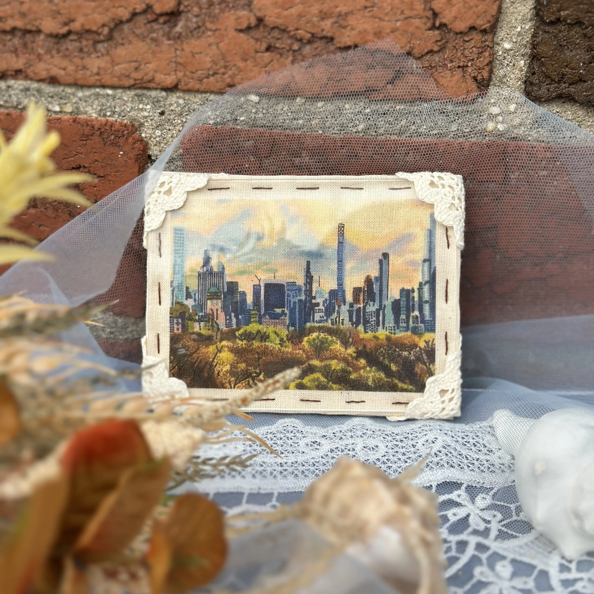 Close-up of a decorative fabric with a city skyline and sunset, seen through a fine mesh screen, with brick wall behind.
