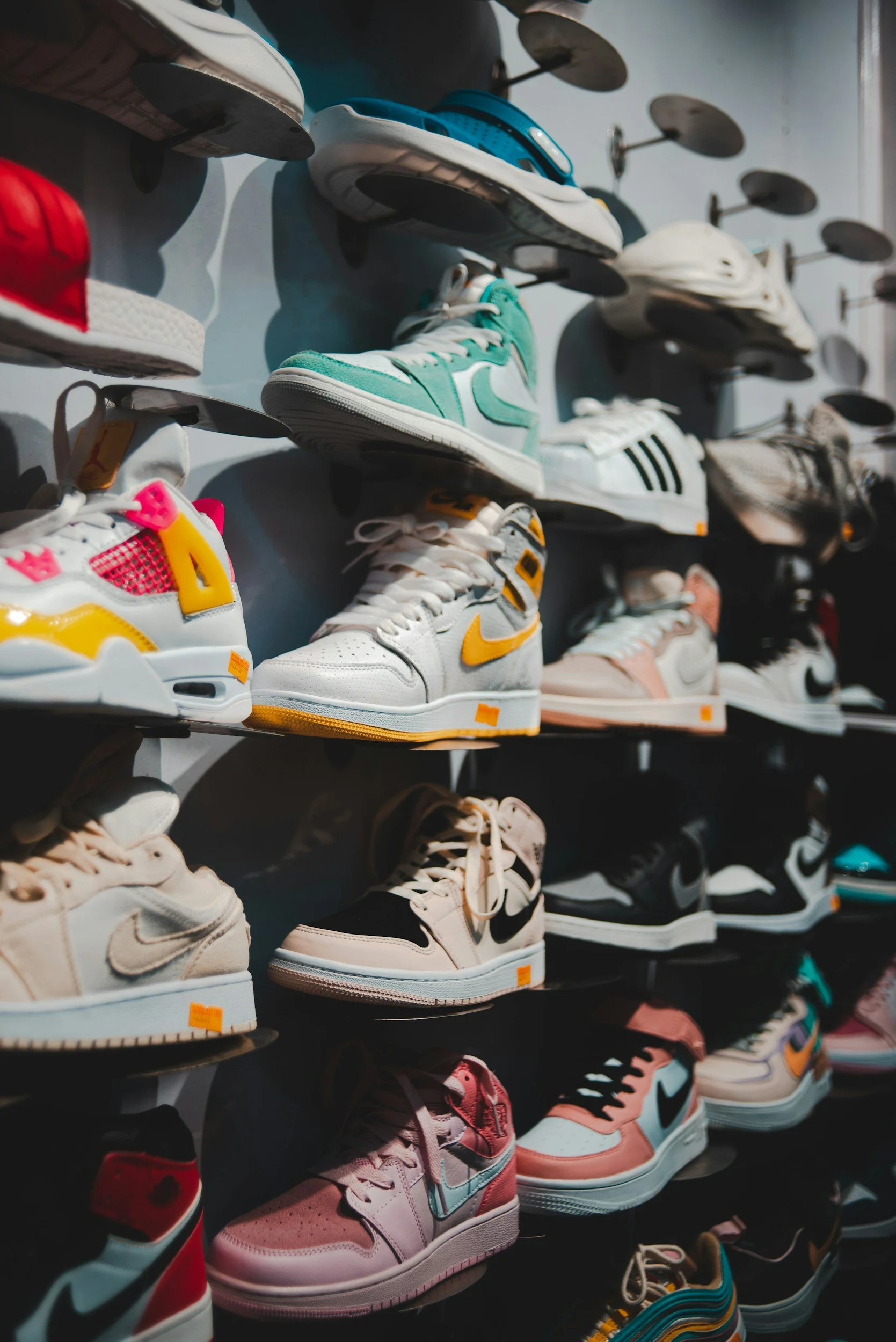 Multiple rows of sneakers and athletic shoes displayed on wall shelves in a shoe store, featuring various colors and styles.