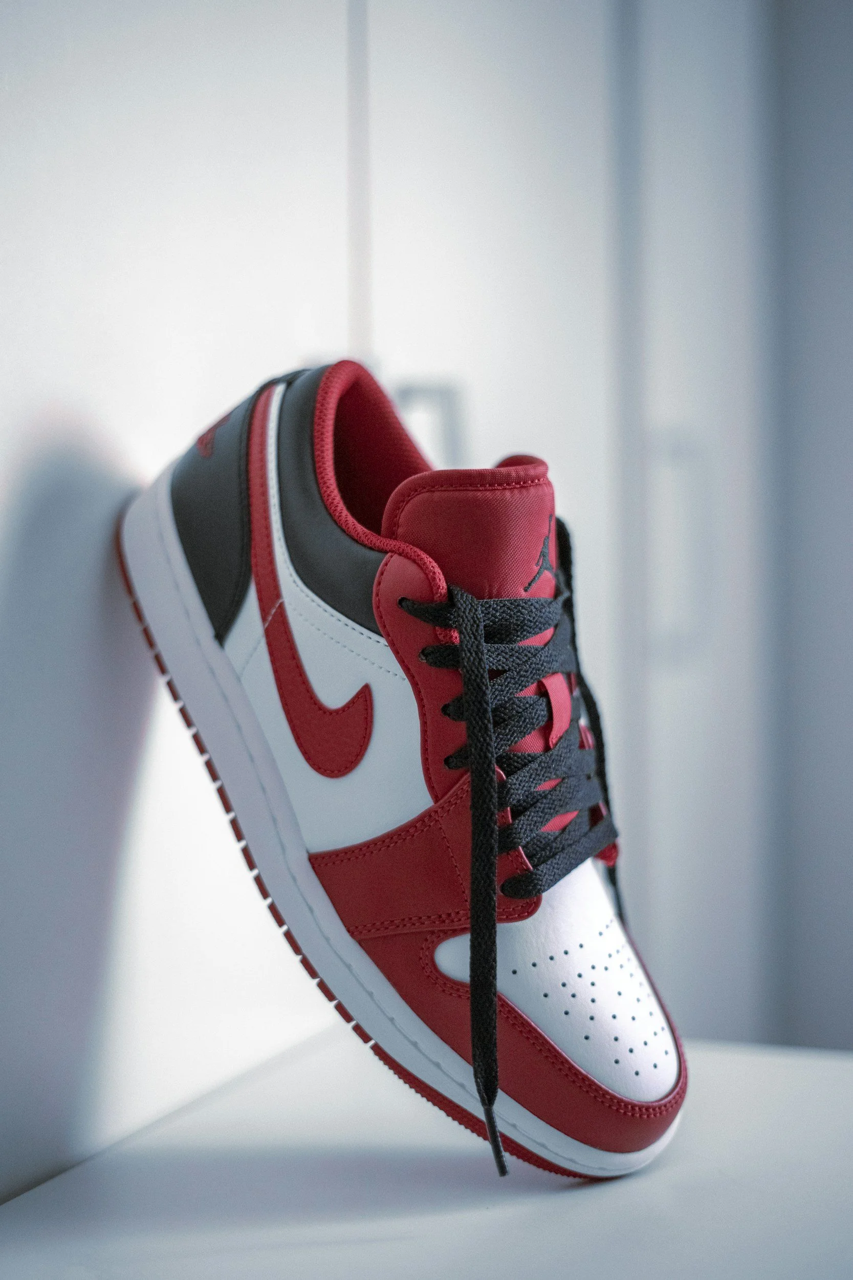 Close-up of a red, black, and white Nike Air Jordan sneaker hanging against a white background.