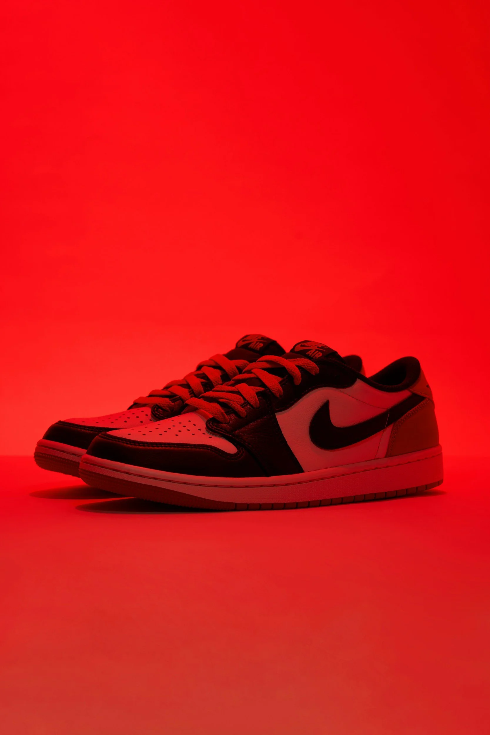 A pair of black and white Nike sneakers with red laces, set against a red background.