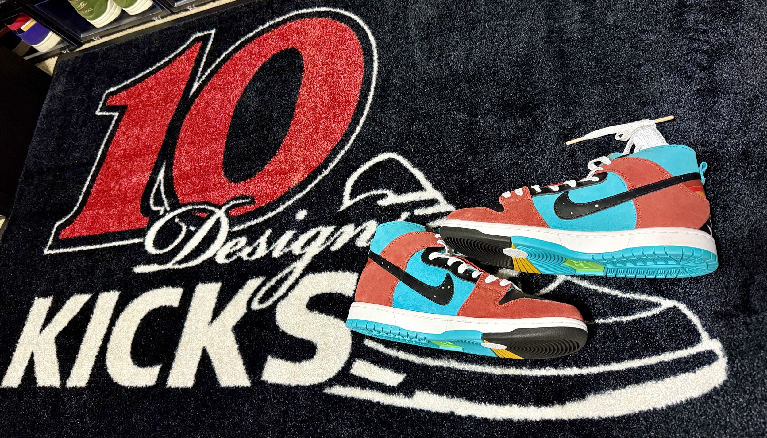 Pair of colorful sneakers with red, blue, black, and yellow accents placed on a black and white carpet with red, black, and white text and design.