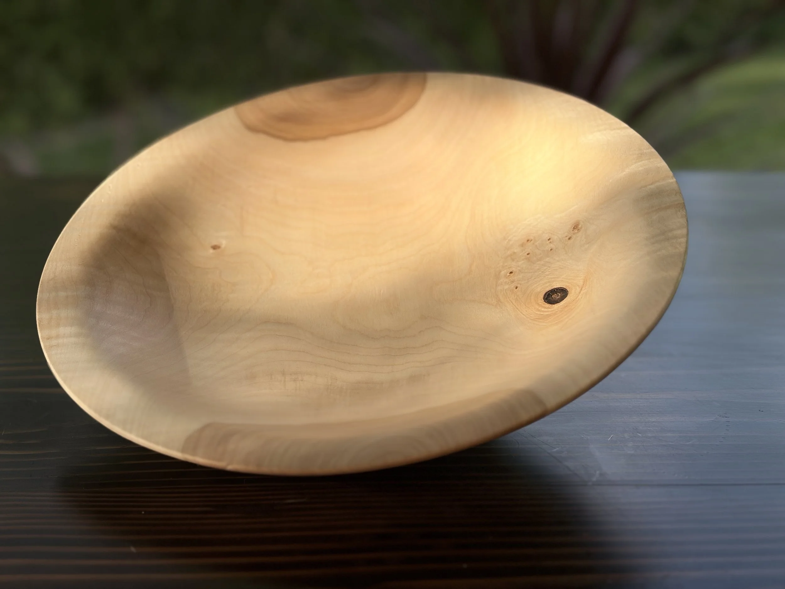 Close-up of a smooth, round, light-colored wooden bowl with visible wood grain, placed on a dark surface with a ridged texture.