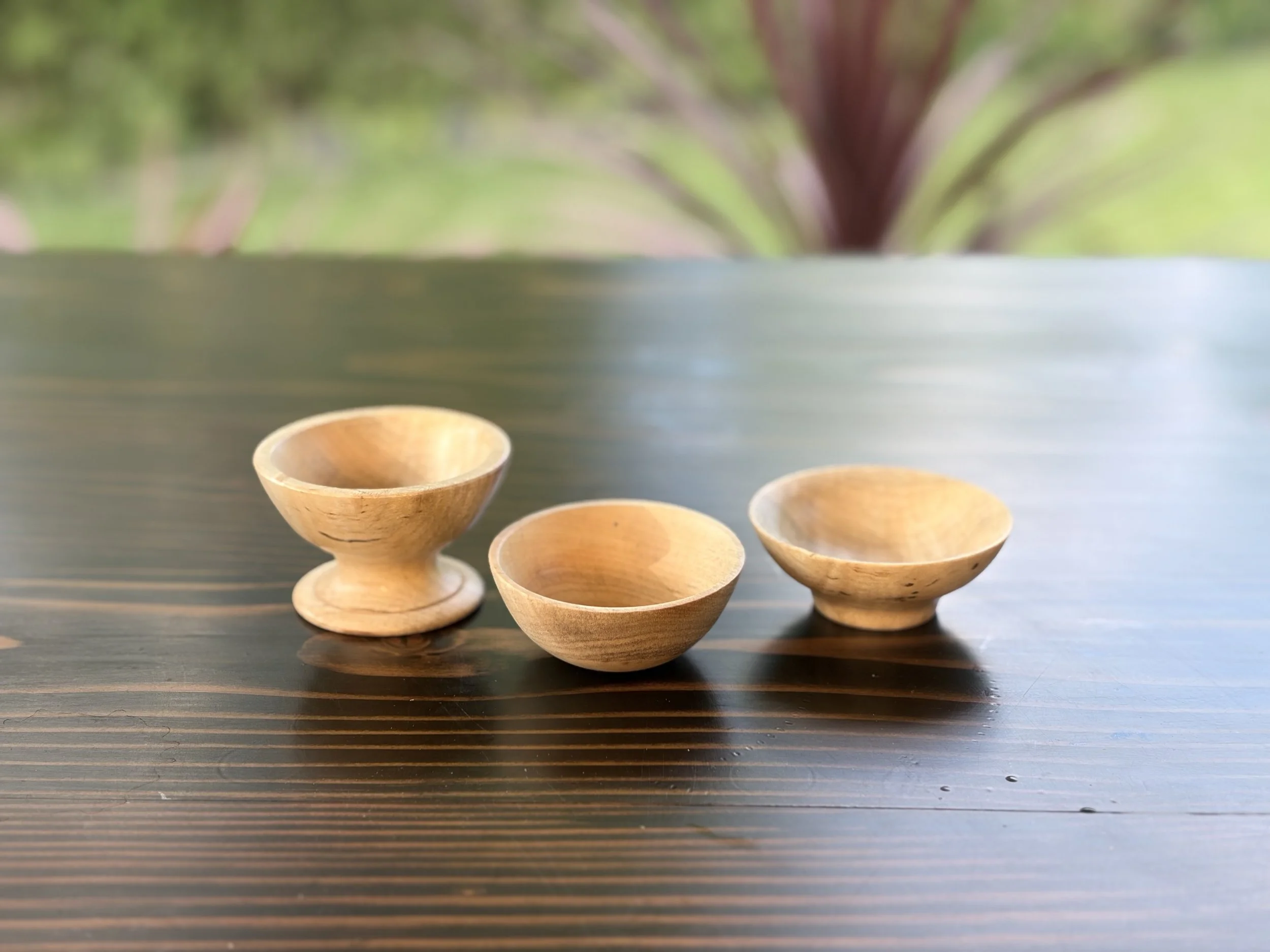 Four wooden bowls placed on a dark wooden table with a blurred green outdoor background.