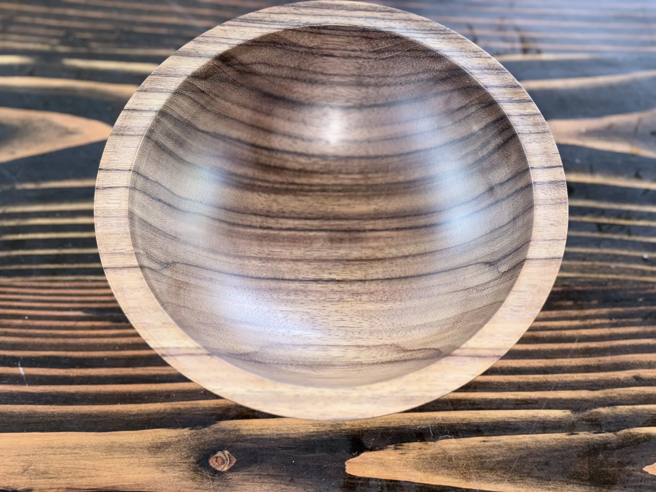 Close-up of a wooden bowl placed on a wooden surface with striped pattern.