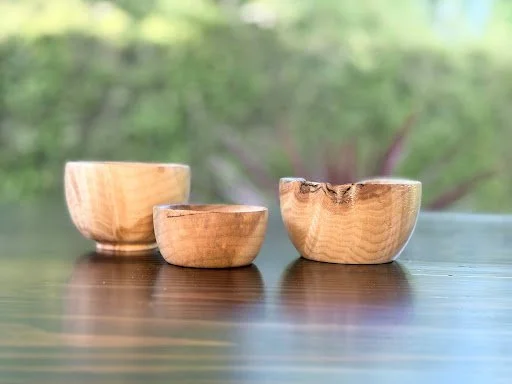 Three wooden bowls of different sizes on a wooden surface with a blurred green outdoor background.