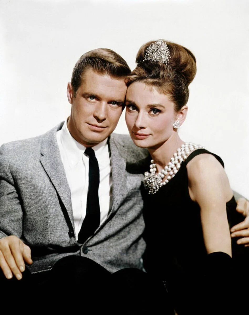 A man and woman dressed in vintage formal clothing, sitting close together on a white background.