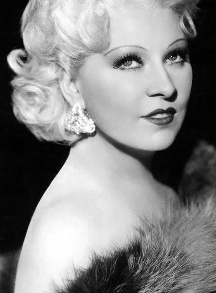 1930s Broadway and Hollywood movie star Mae West in a studio publicity photo wearing diamond earrings and furs.