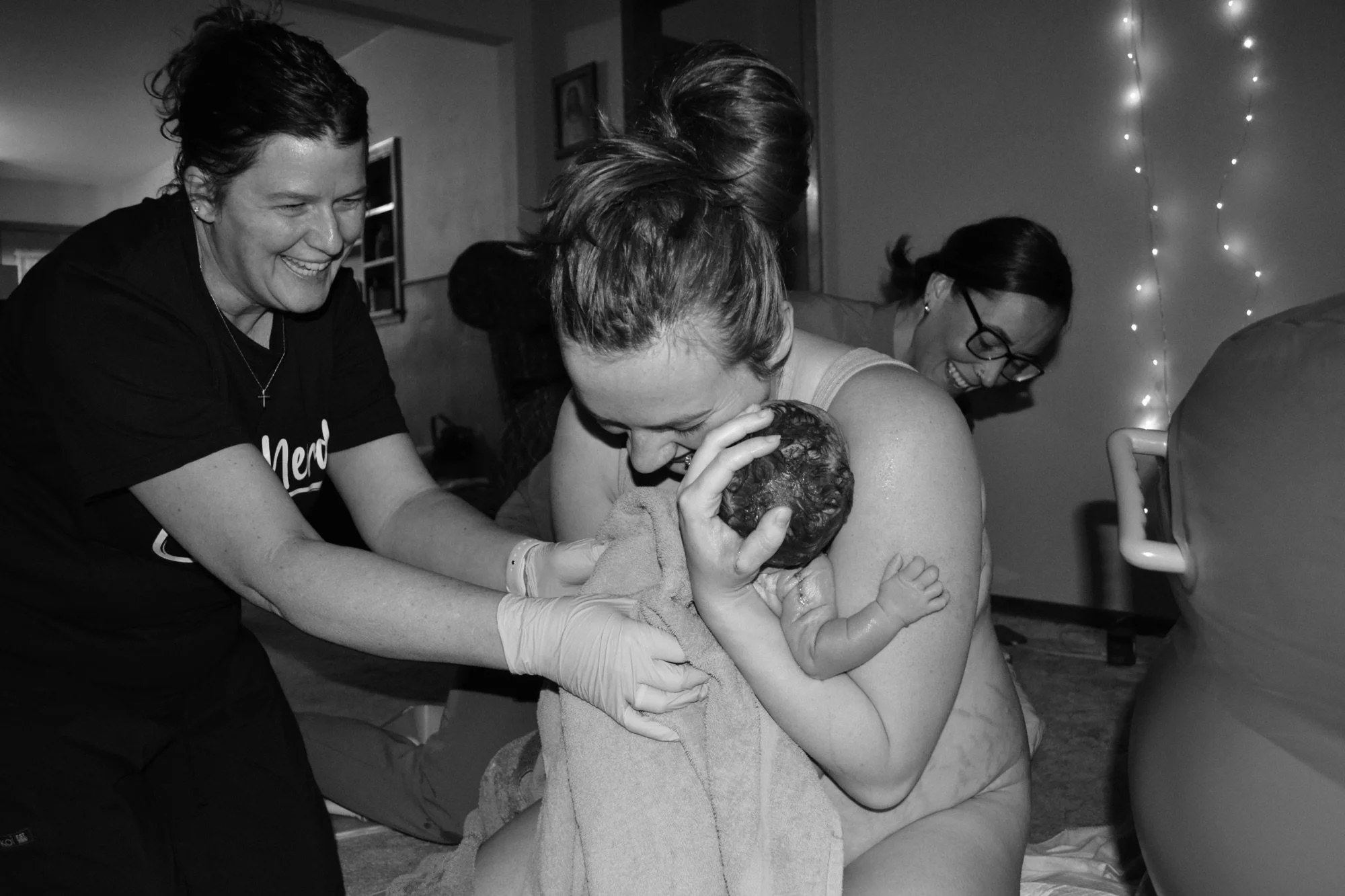 A woman holding a newborn baby while two women look on and smile during a home water birth or birth center birth.