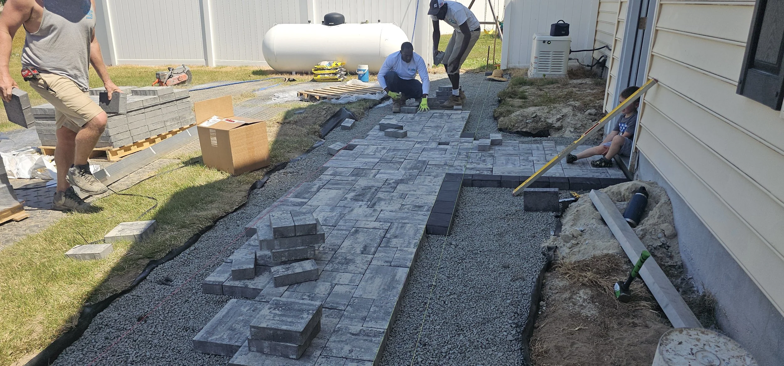 Delaware Grading Services laying down paving stones to create a walkway next to a house.