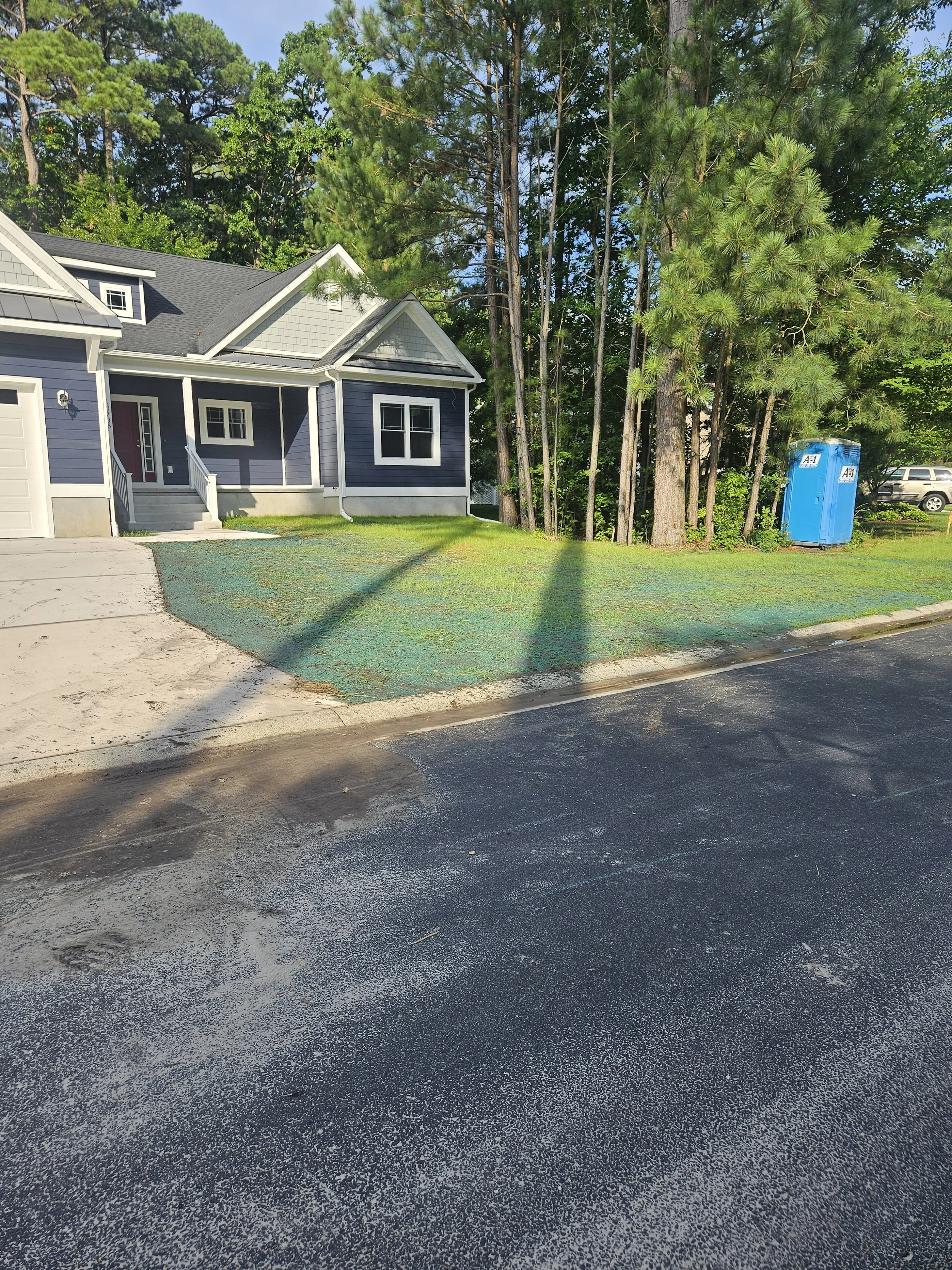 Residential front yard with a house, trees, a portable toilet, and a parked vehicle in the background. showcasing new grass seed planted  Delaware Grading Services